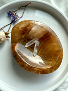 Golden Healer crystal bowl used as a jewelry or charging dish, overhead view with quartz points inside, white background with floral styling