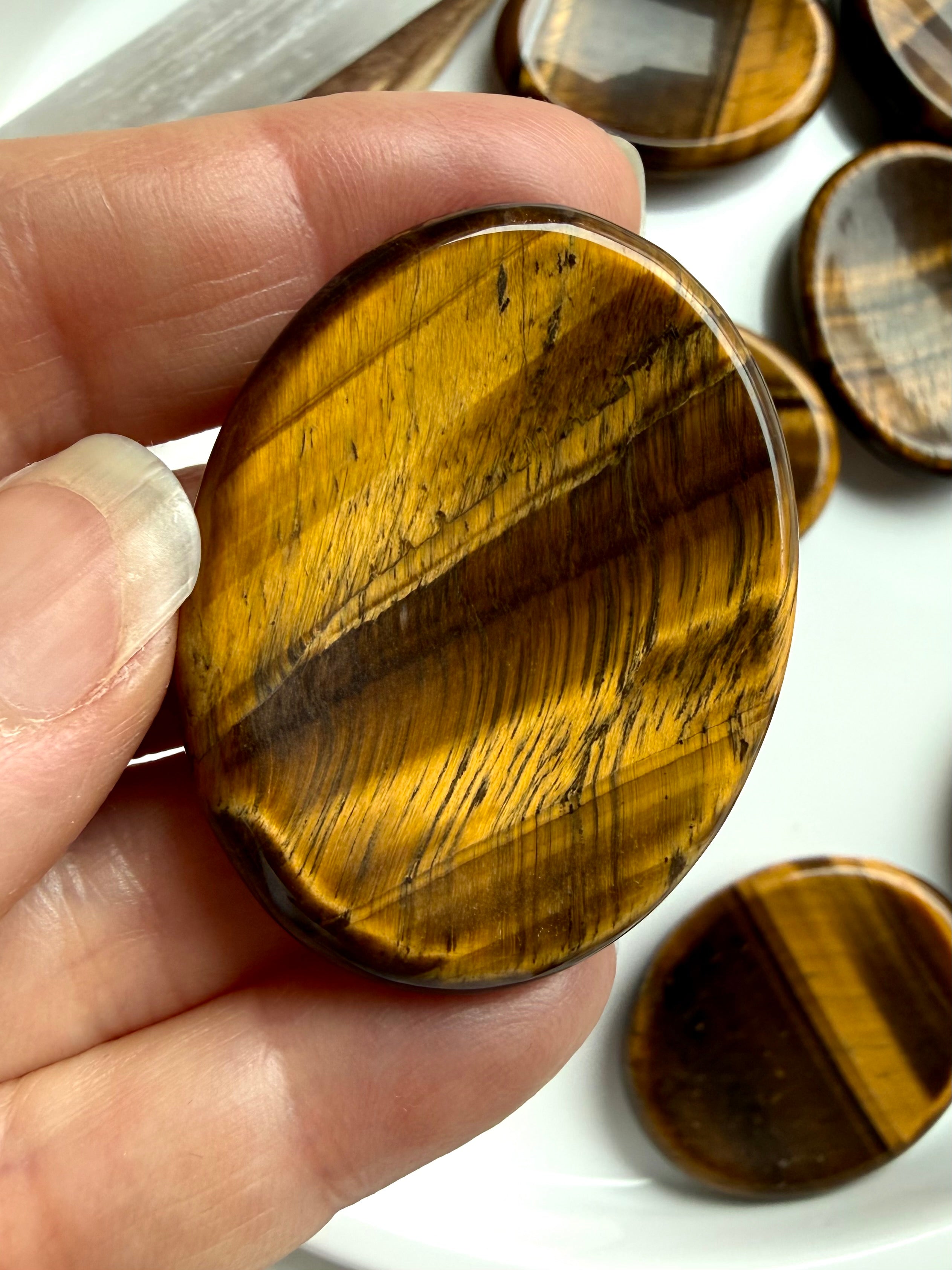 tiger’s eye worry stone held between fingers showing natural banding and sheen, crystal for protection strength and balance