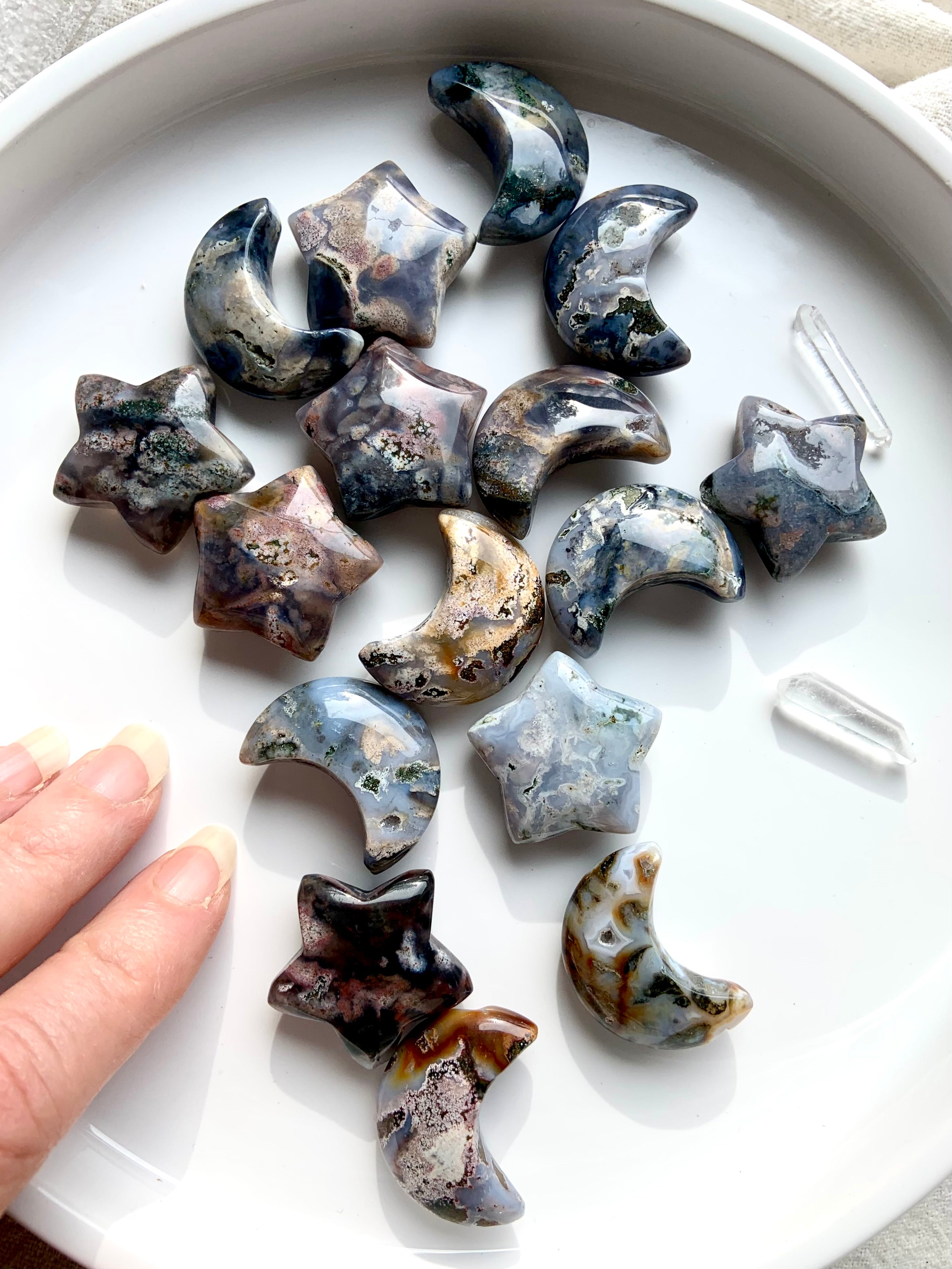 Cosmic Ocean Jasper moons and stars with quartz points on white dish and hand reaching in, celestial healing crystal carvings for rituals