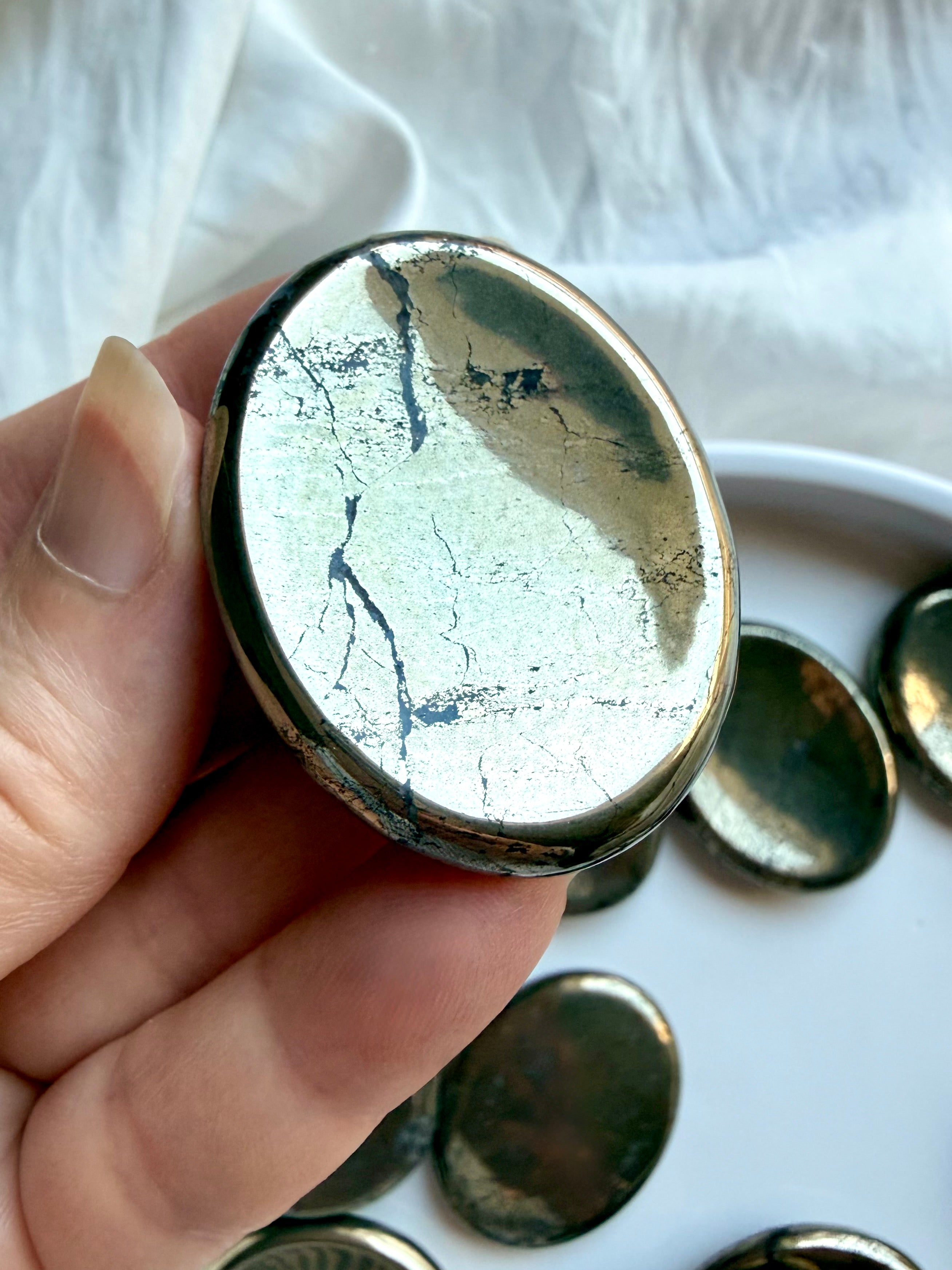 Polished Pyrite thumb stone held in hand with bright metallic luster and natural mineral patterning