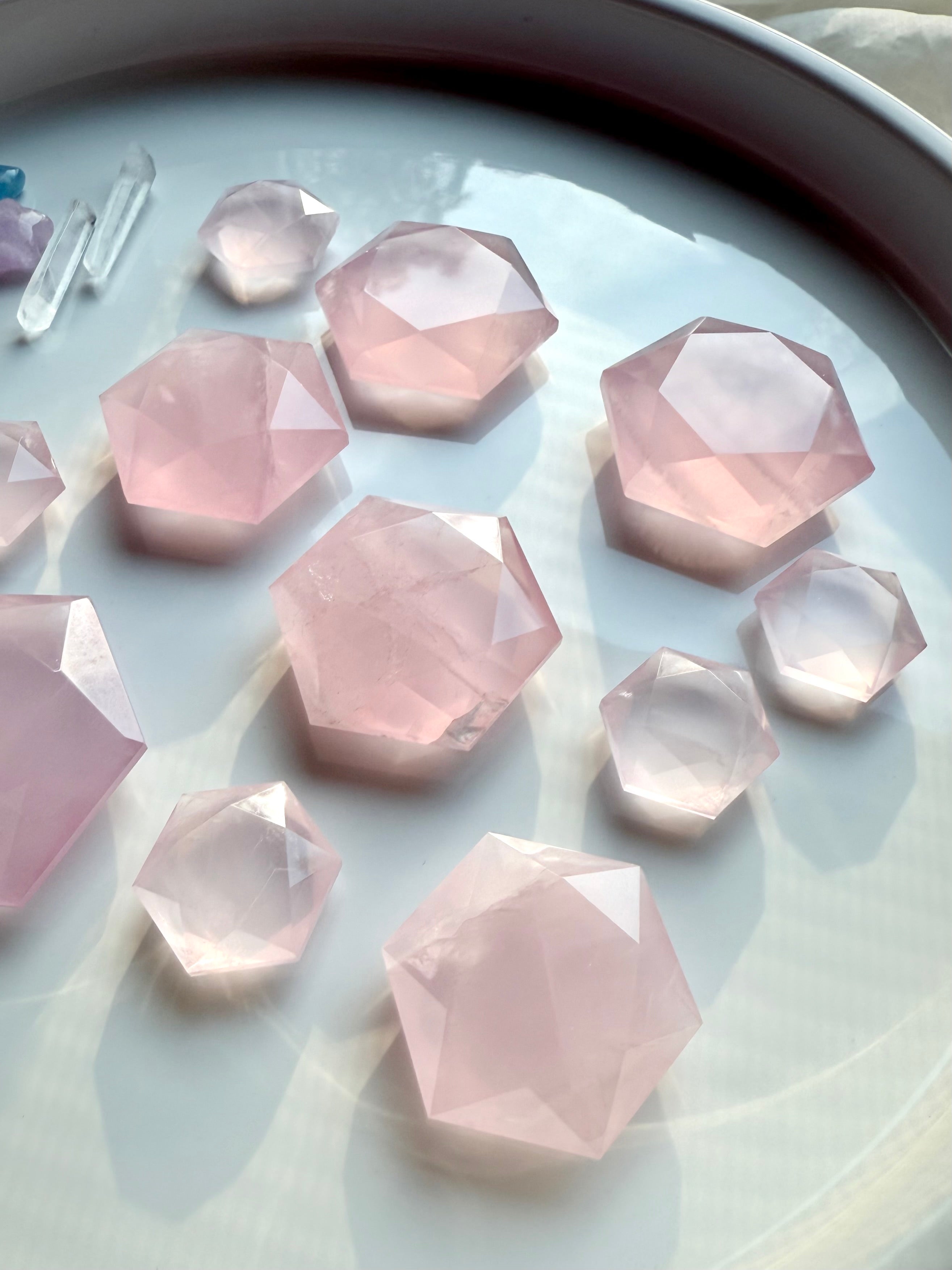 Several sizes of faceted rose quartz crystal hexagons on white, Heart Chakra crystals with natural veining &amp; soft pink color