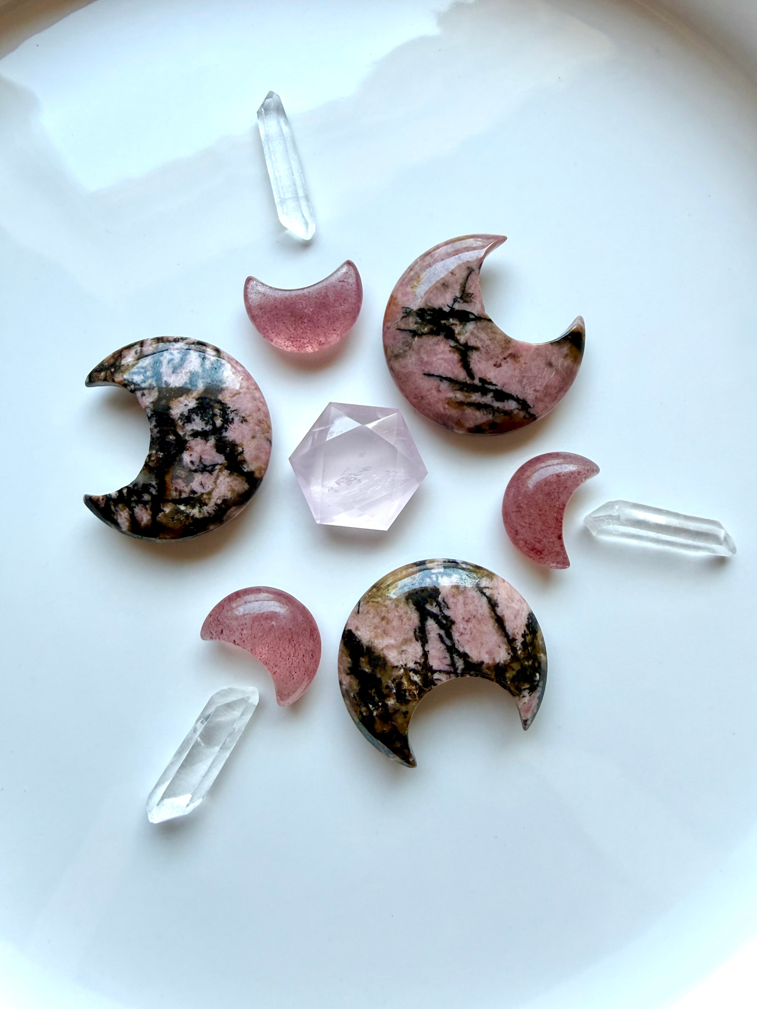 Rhodonite and Strawberry Quartz crescent moon crystals with a Rose Quartz hexagon and Clear Quartz points on a white display plate