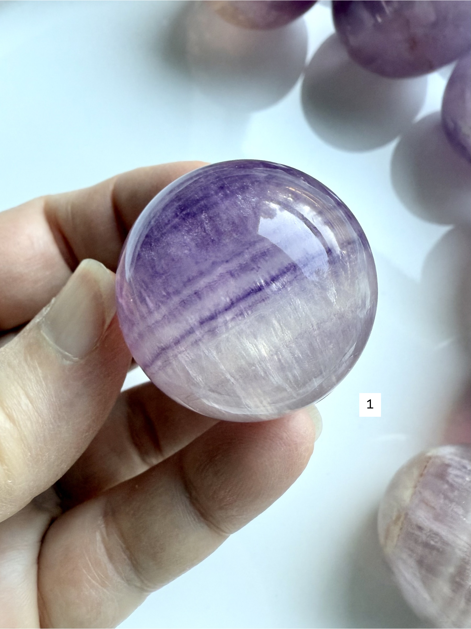 hand holding Silky Magenta Fluorite sphere with luminous purple banding and glossy polished finish
