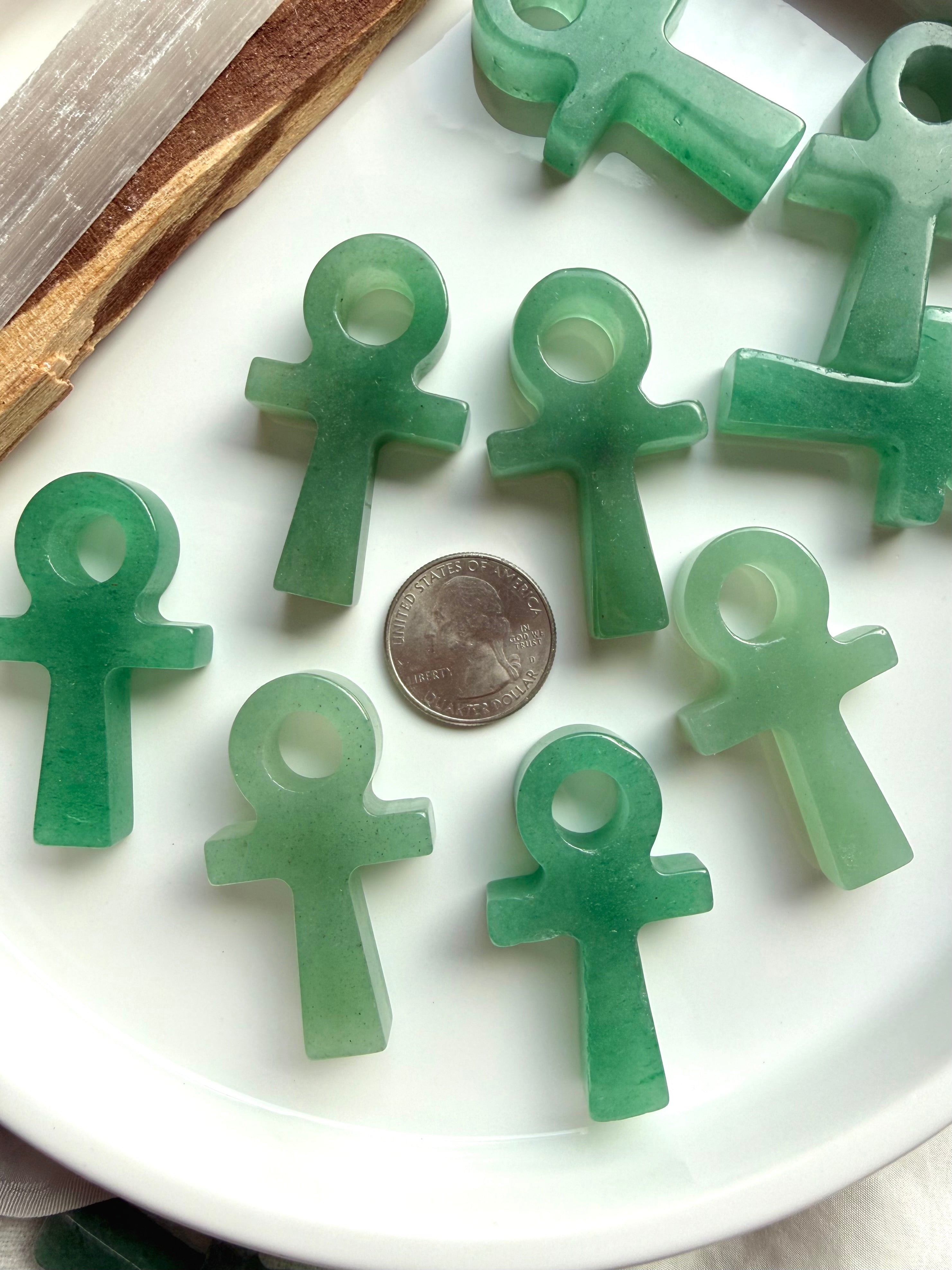 Assorted green aventurine ankh carvings with natural variation shown with a US quarter for scale