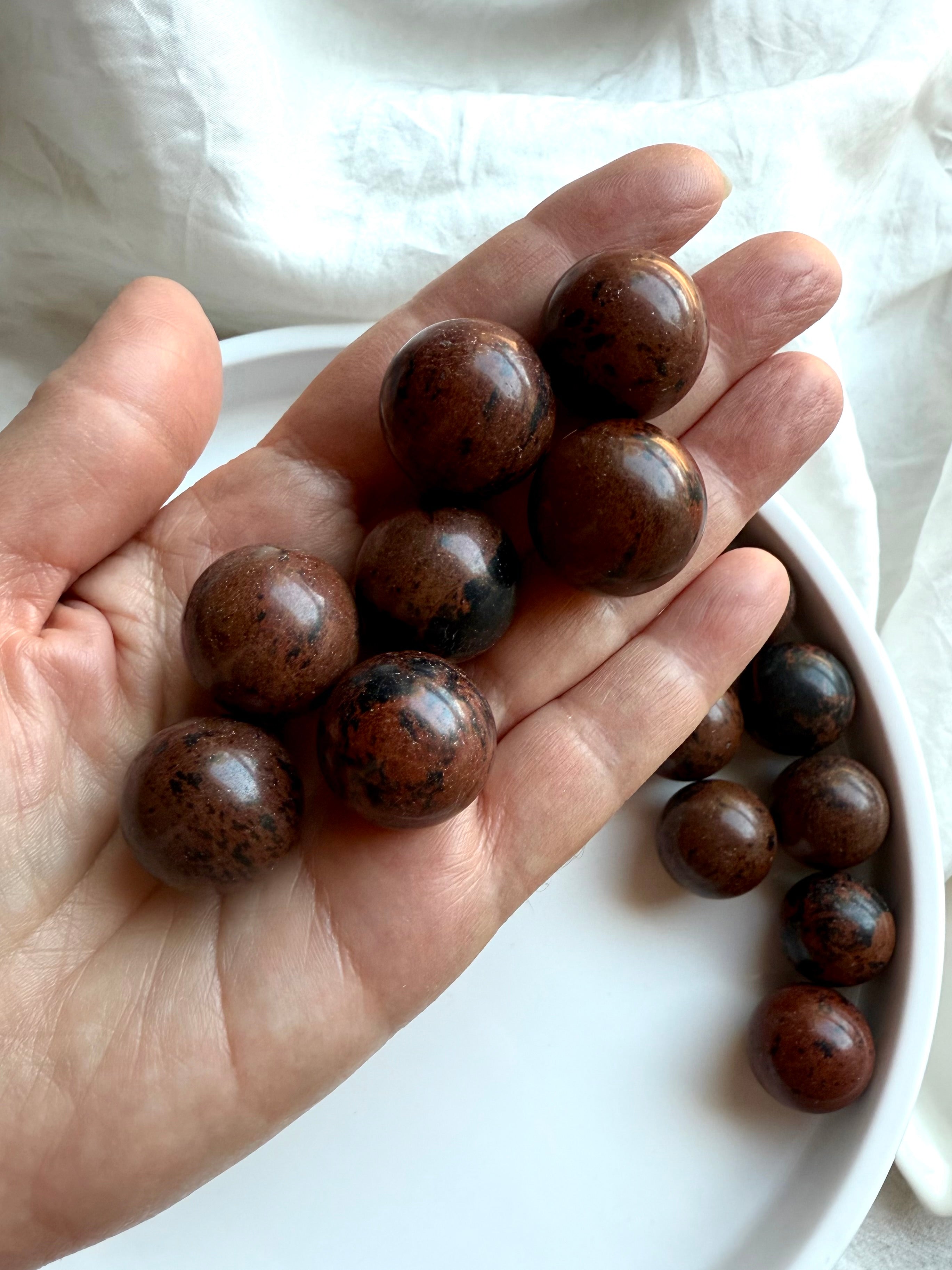 Hand holding polished Mahogany Obsidian spheres – healing crystals for Root Chakra balance and energy protection