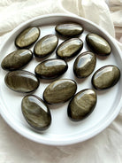 Golden Sheen Obsidian palm stones arranged together showing varied gold, bronze and silvery sheen across glossy black surfaces