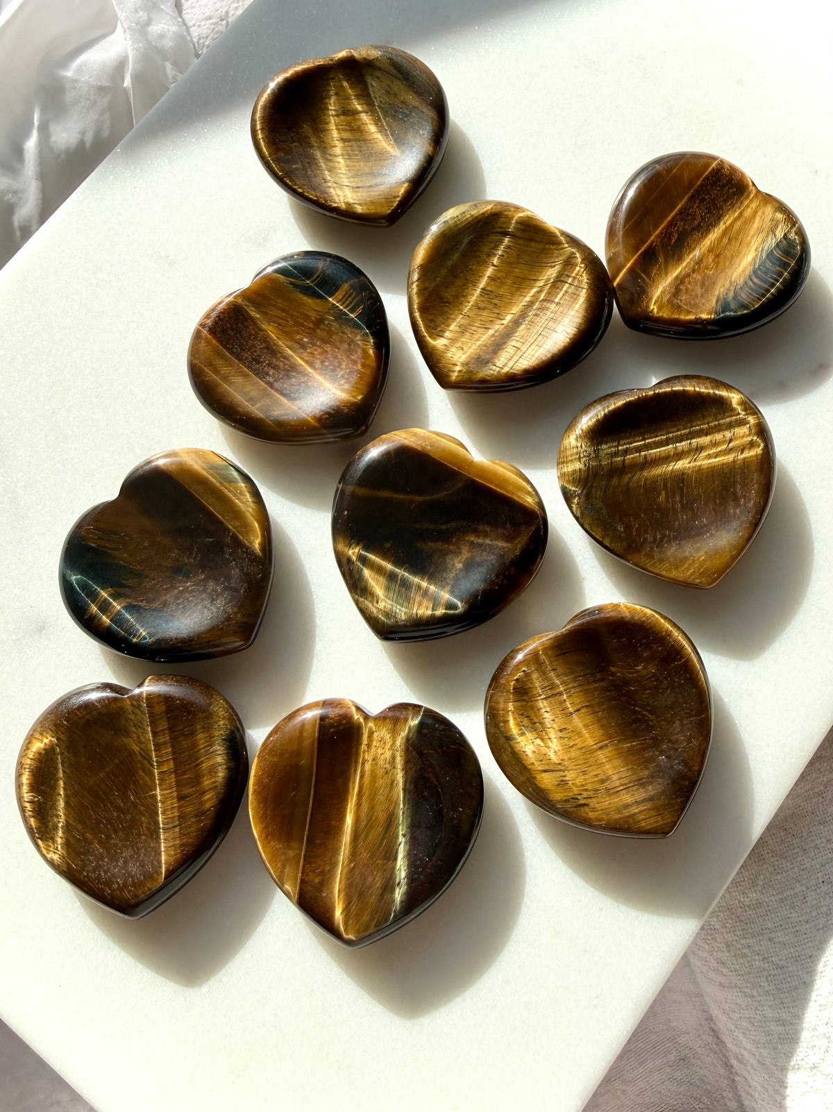 Collection of Tiger’s Eye heart worry stones with golden and bronze bands, polished heart shapes, and smooth thumb indentations
