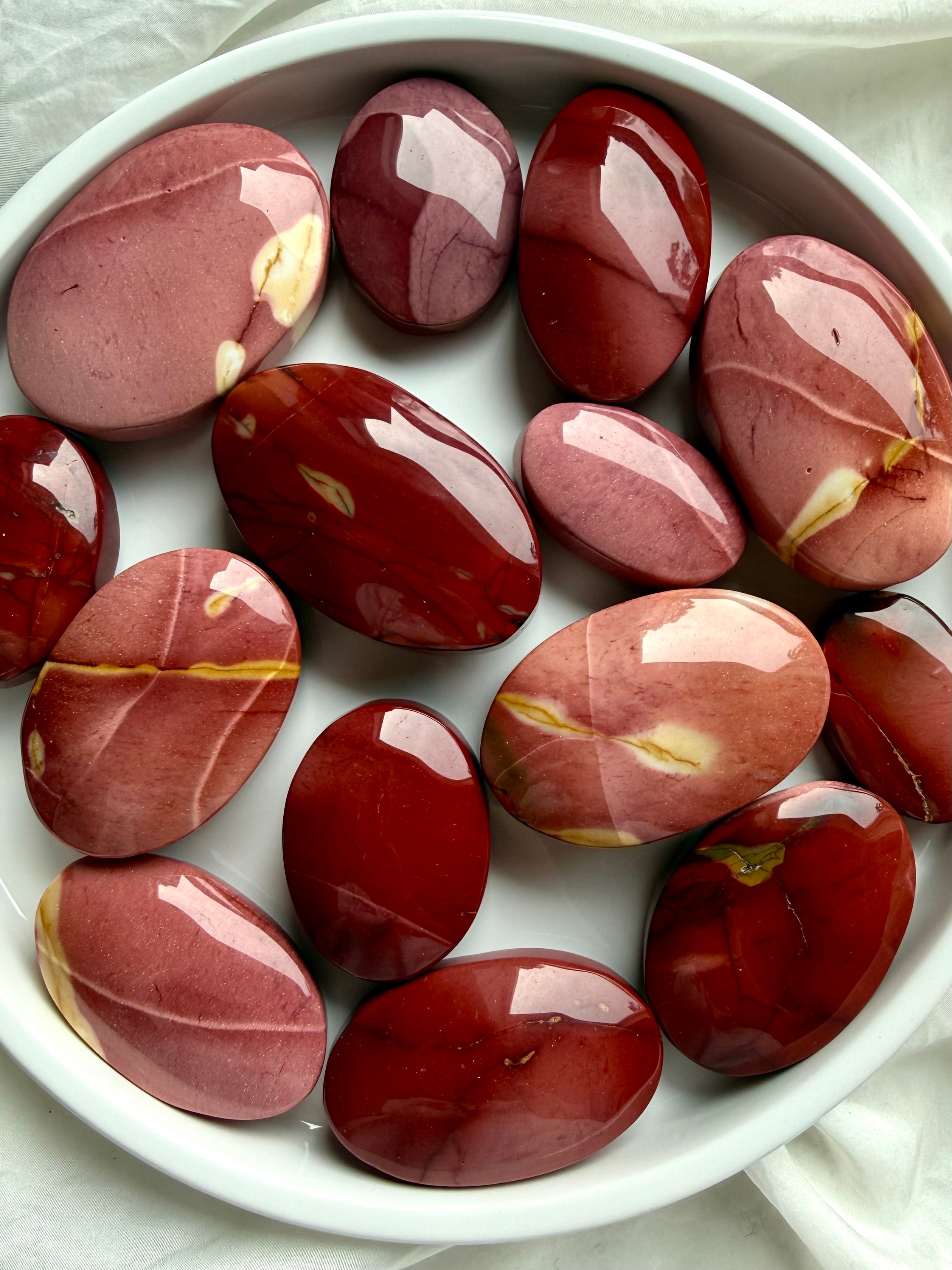 Mookaite Jasper palm stones arranged in white bowl showing natural red, burgundy, and blush color variations