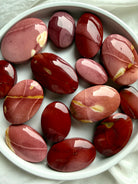 Mookaite Jasper palm stones arranged in white bowl showing natural red, burgundy, and blush color variations