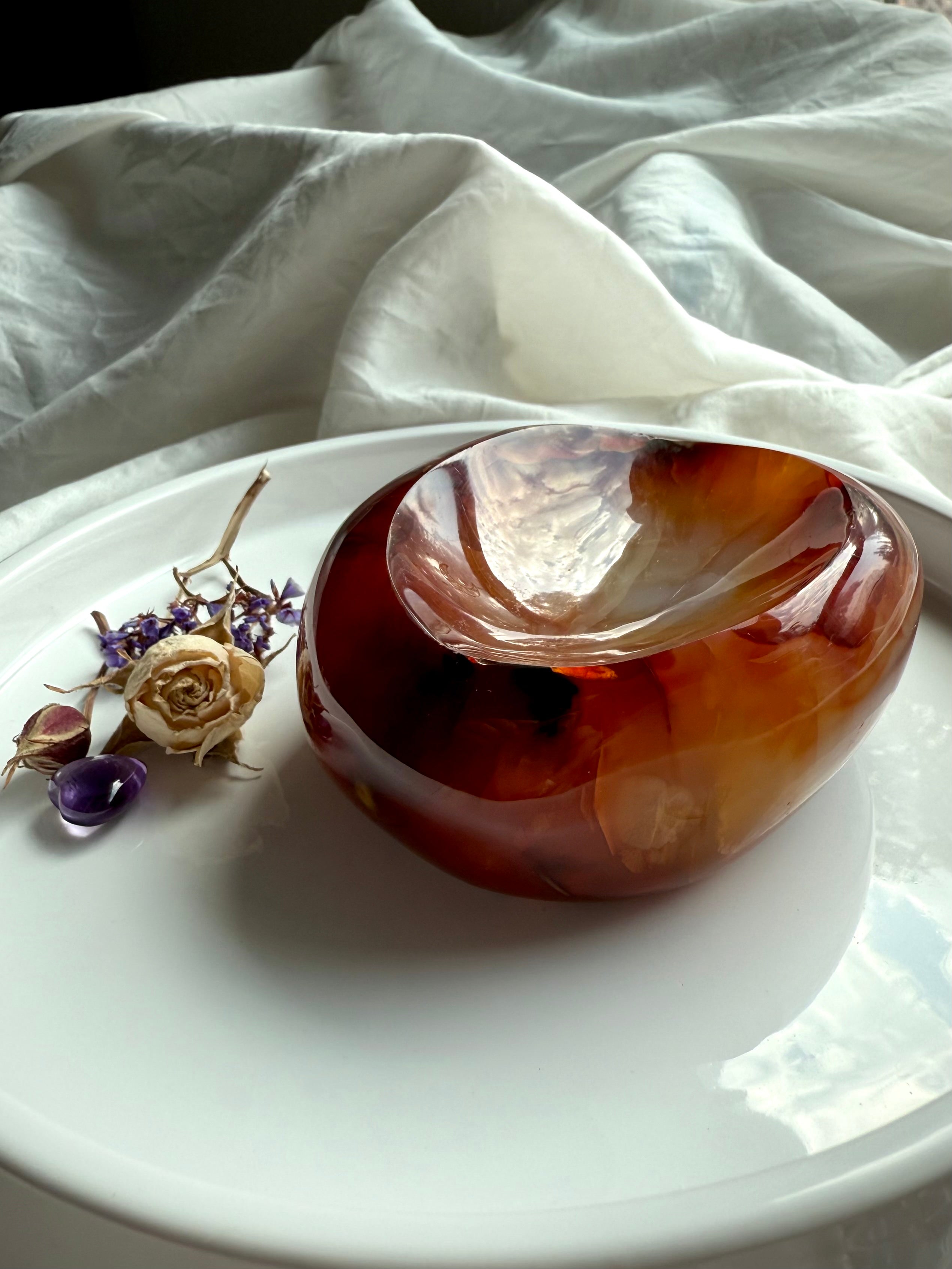 Carnelian crystal bowl on white plate with dried flowers, glowing with deep red and golden patterns.