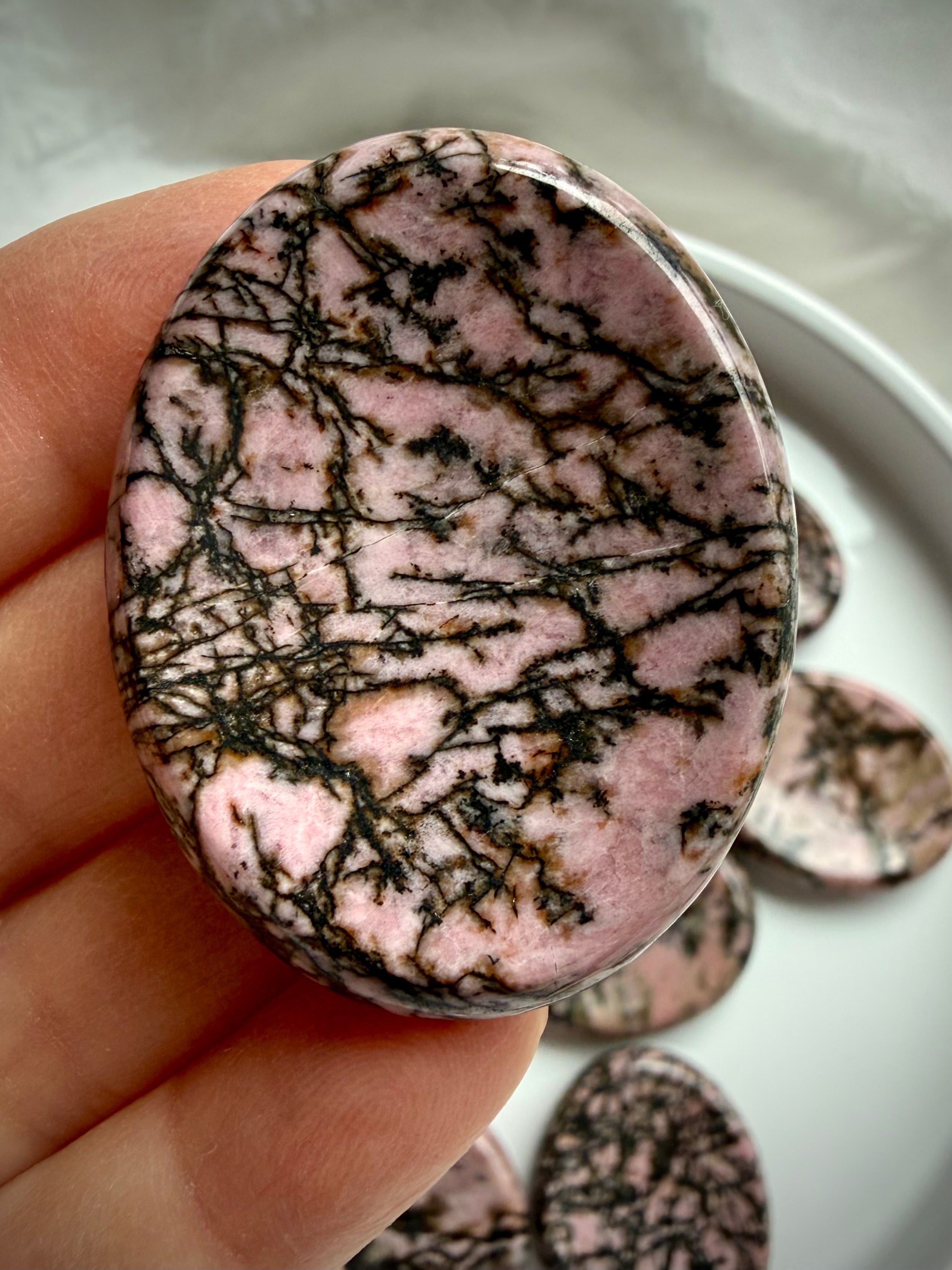 Rhodonite worry stone in hand showing varied black spiderweb patterns running through pink matrix