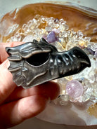 silver sheen obsidian dragon carving displayed on shell dish of crystals highlighting reflective sheen, crystal for shadow work and intuition