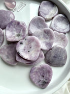 An array of Lepidolite heart thumb stones with lavender purple mottling and natural inclusions