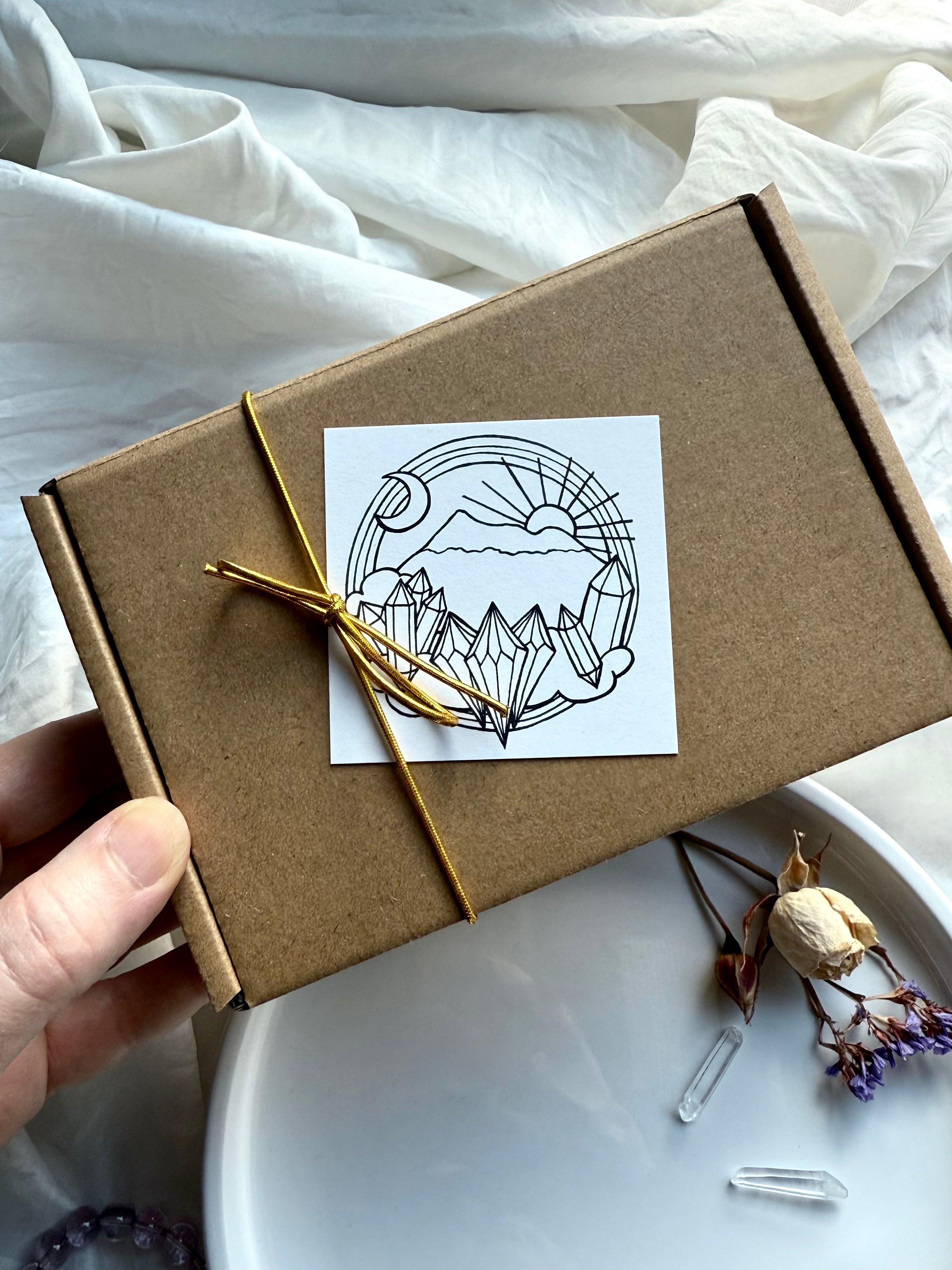Hand holding kraft gift box with golden cord and celestial crystal-themed sticker label