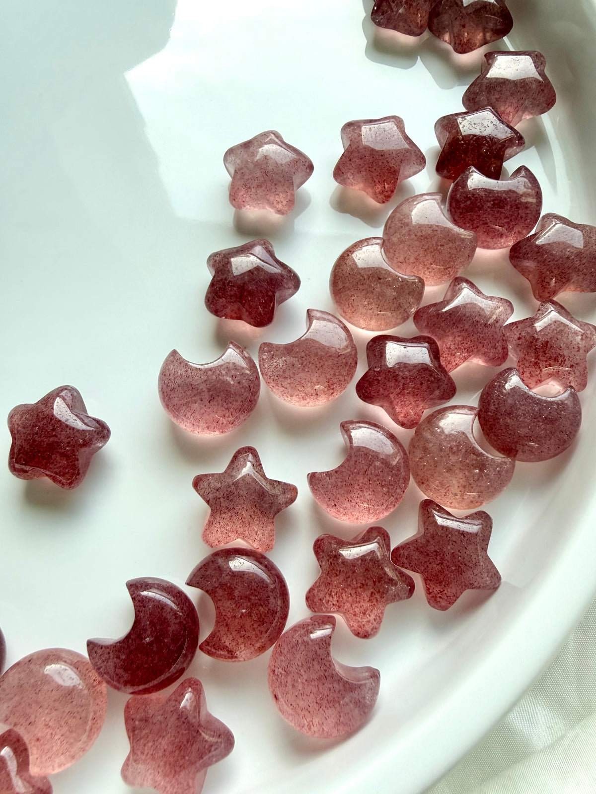 Strawberry Quartz moon and star crystals arranged on a white tray, featuring rich red, soft pink and translucent gemstone carvings