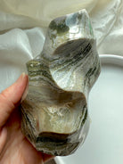 Side view of Green Ocean Jasper flame showing layered forest-green and cream patterns in a smooth freeform sculpture. 