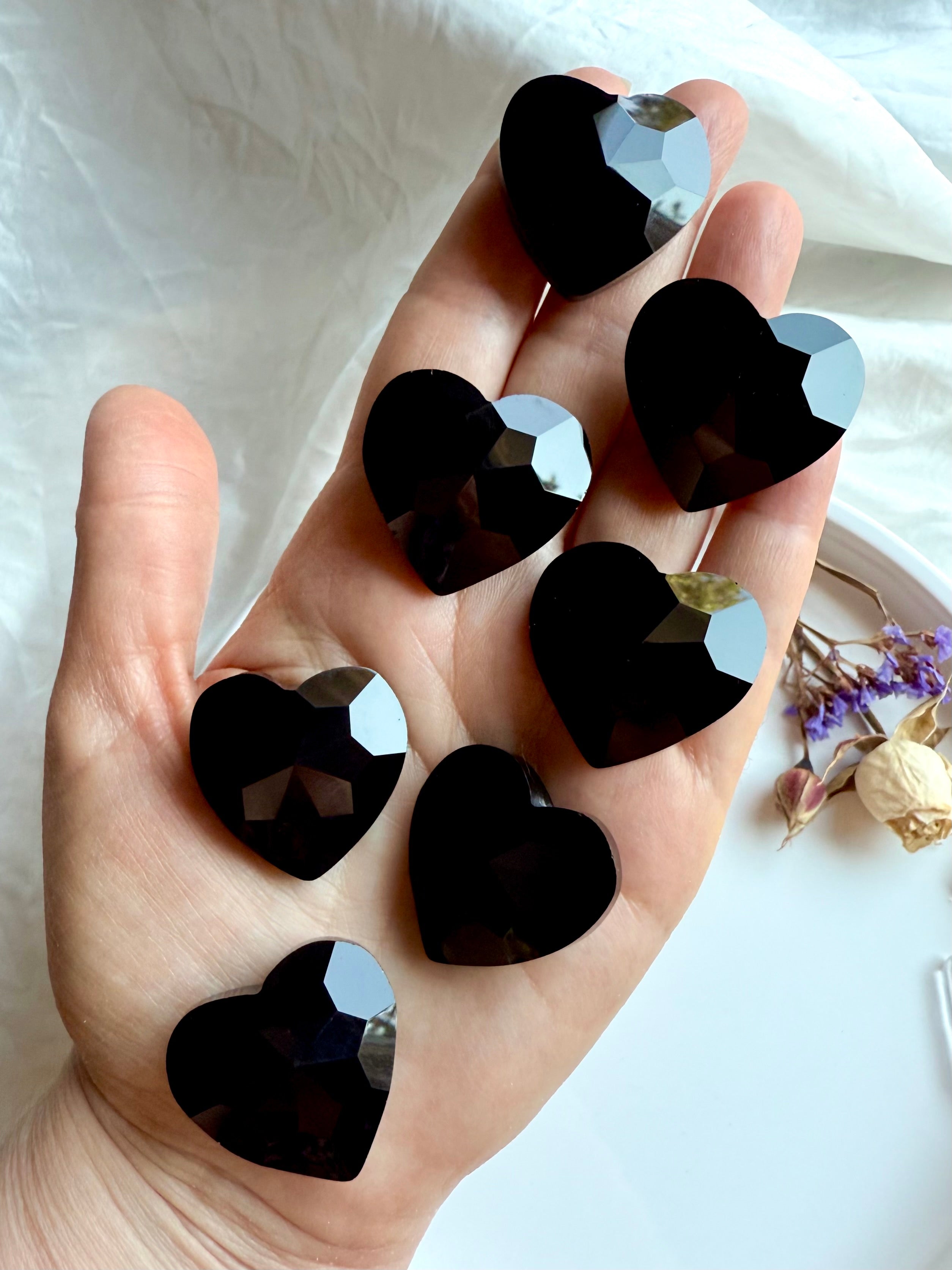 Black obsidian heart carvings shown on hand for scale. Root chakra crystals for energetic protection.
