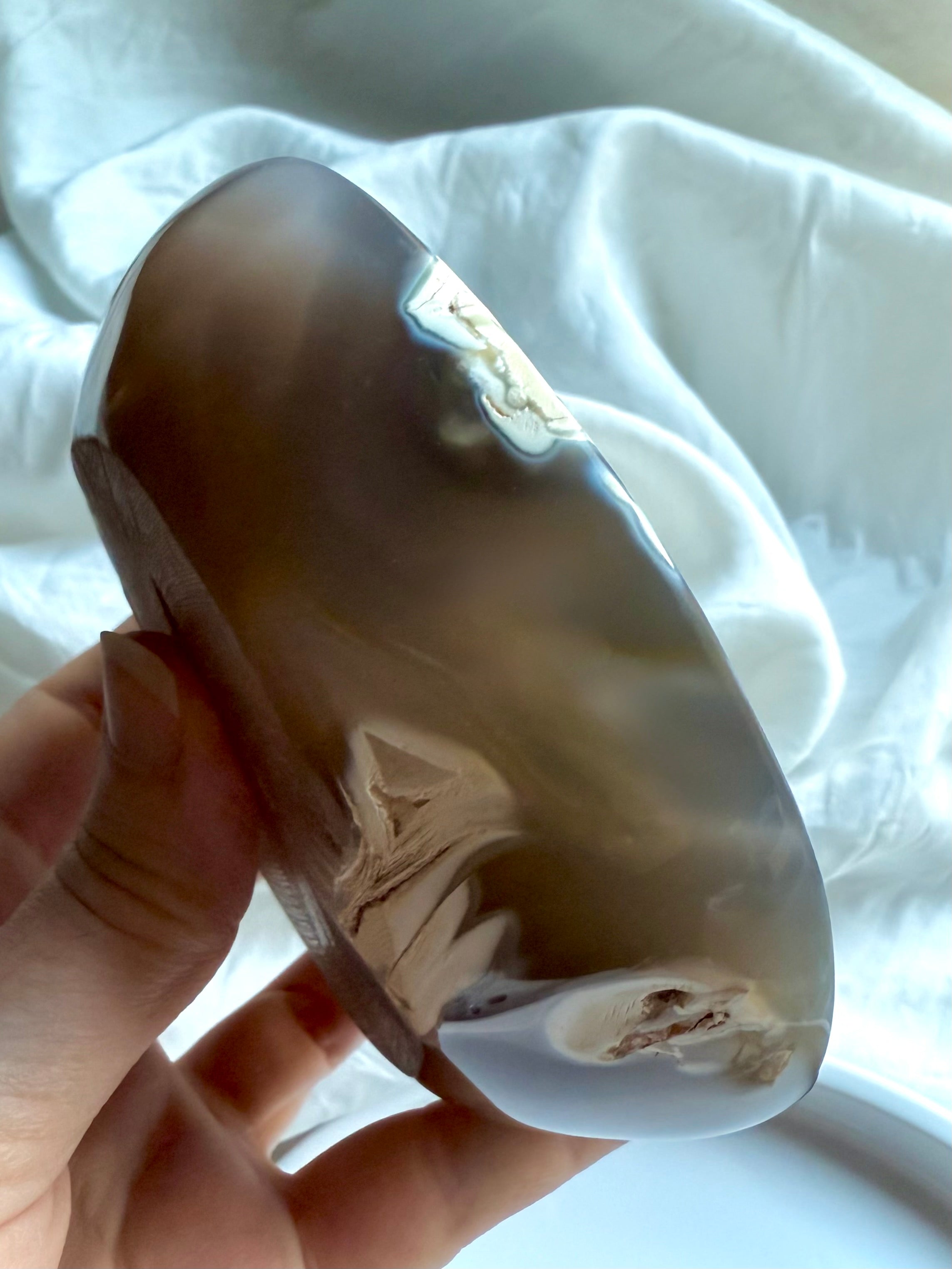 Hand holding polished Orca Agate bowl from a side angle, showing its smooth curved edge and soft grey translucence