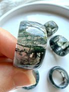 hand holding chunky moss agate wide band ring with natural translucent inclusions and polished glossy finish