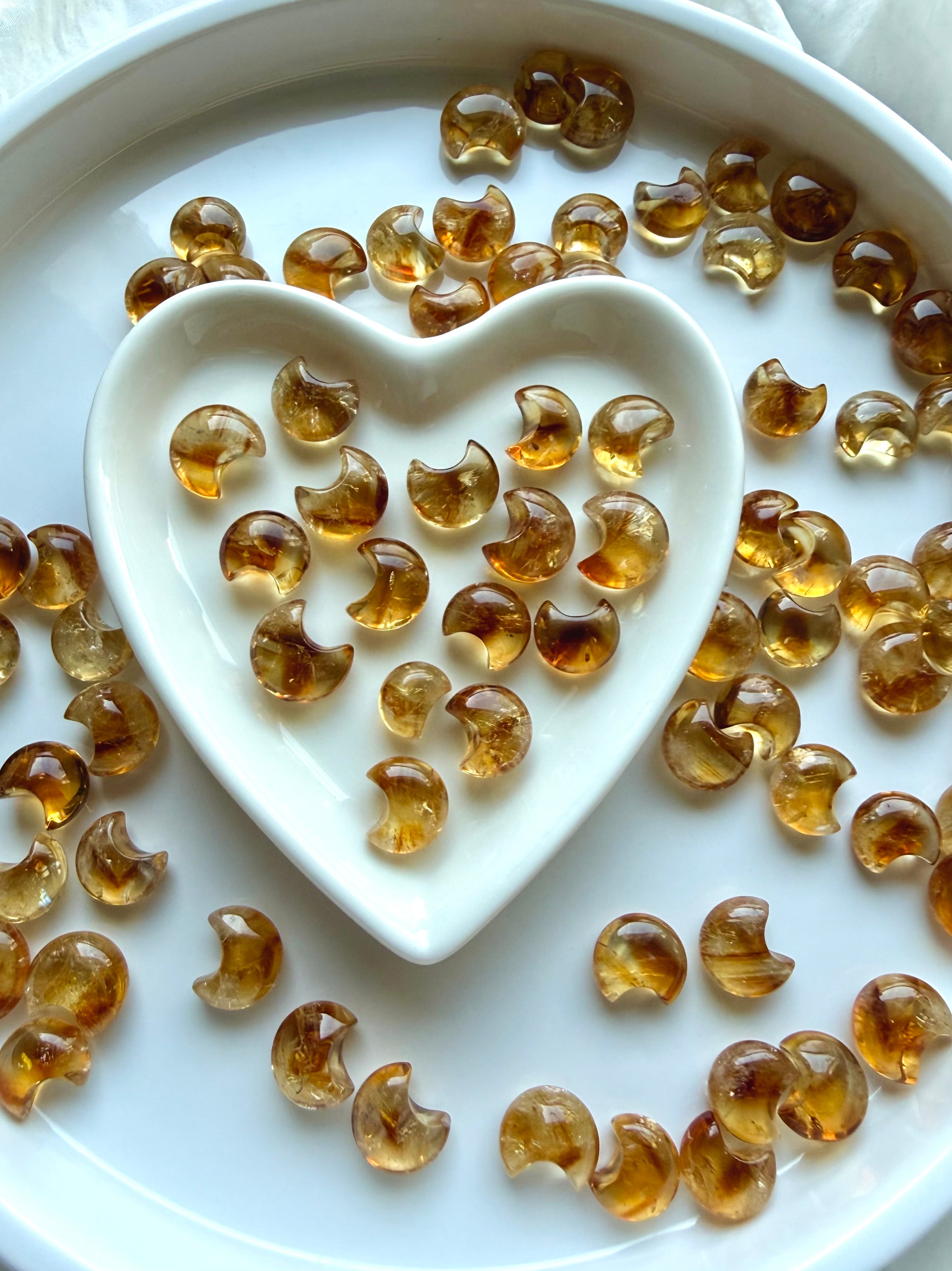 Mini Citrine moons arranged around a white heart-shaped dish showing their range of golden honey and amber color