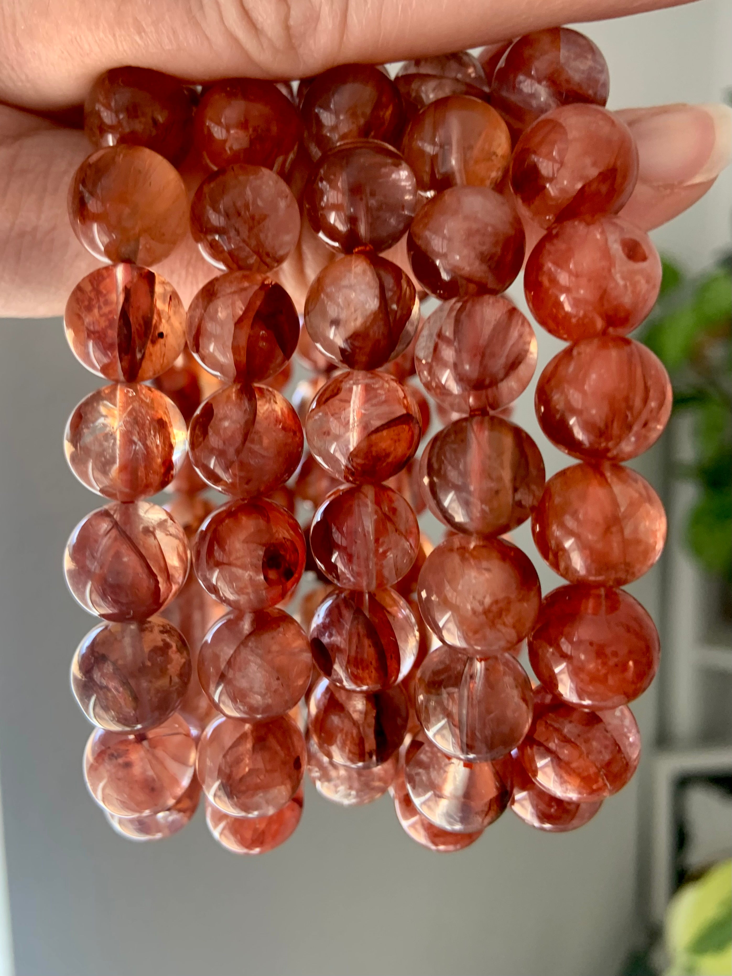 Several Fire Quartz crystal bracelets held to the light, showing red Hematoid Quartz beads in 11.2mm and 11.8mm sizes with natural clarity and color