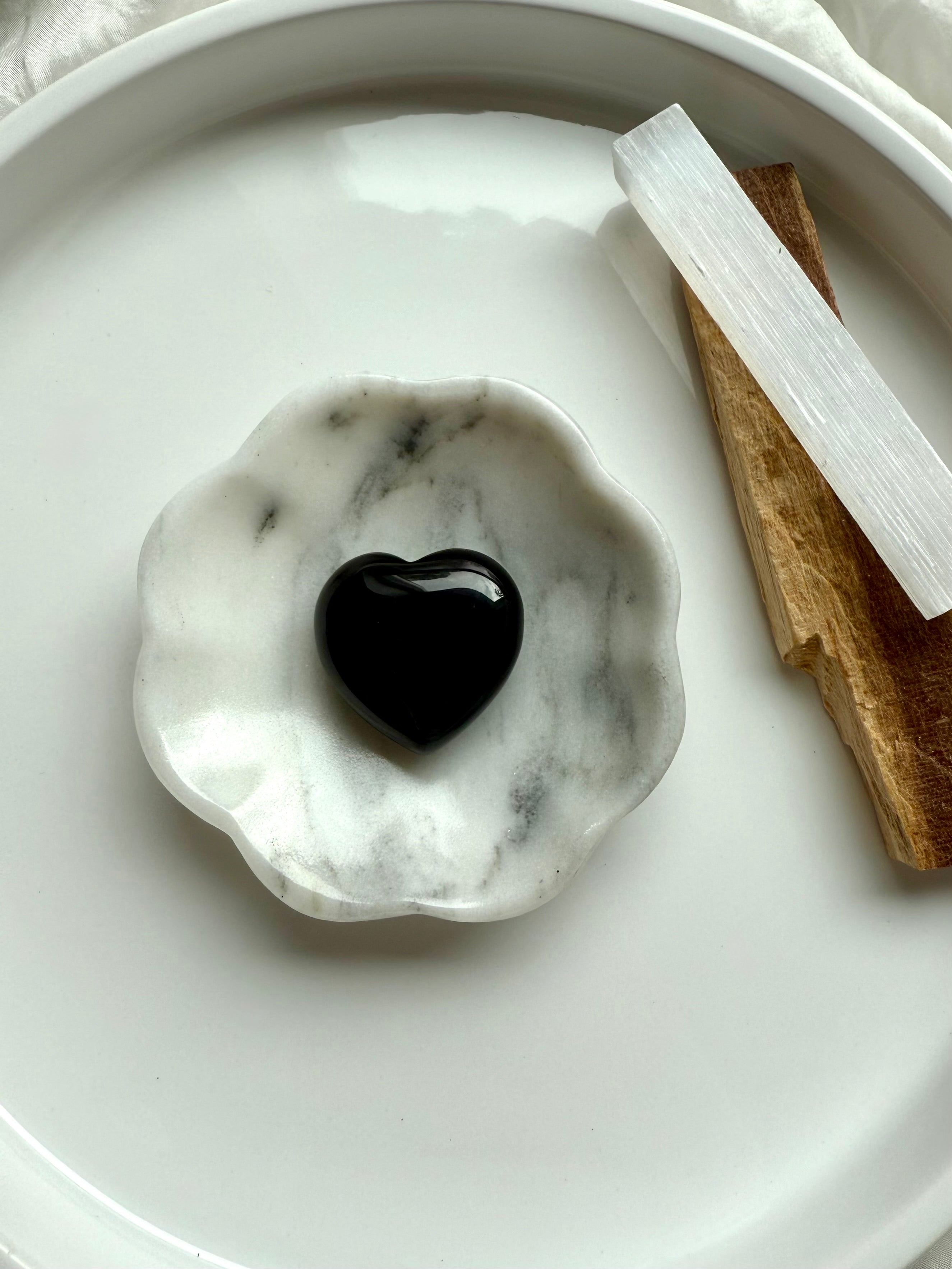 Black Obsidian heart displayed in a white marble flower-shaped dish with selenite and palo santo.