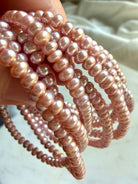 closeup of multiple pink pearl bracelets draped in hand, soft lilac freshwater pearl jewelry stack with natural sheen and feminine energy