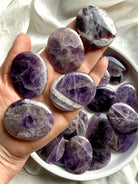 Dream amethyst palm stones shown on hand highlighting slim flat shape, smooth polish, and pocket-friendly thickness