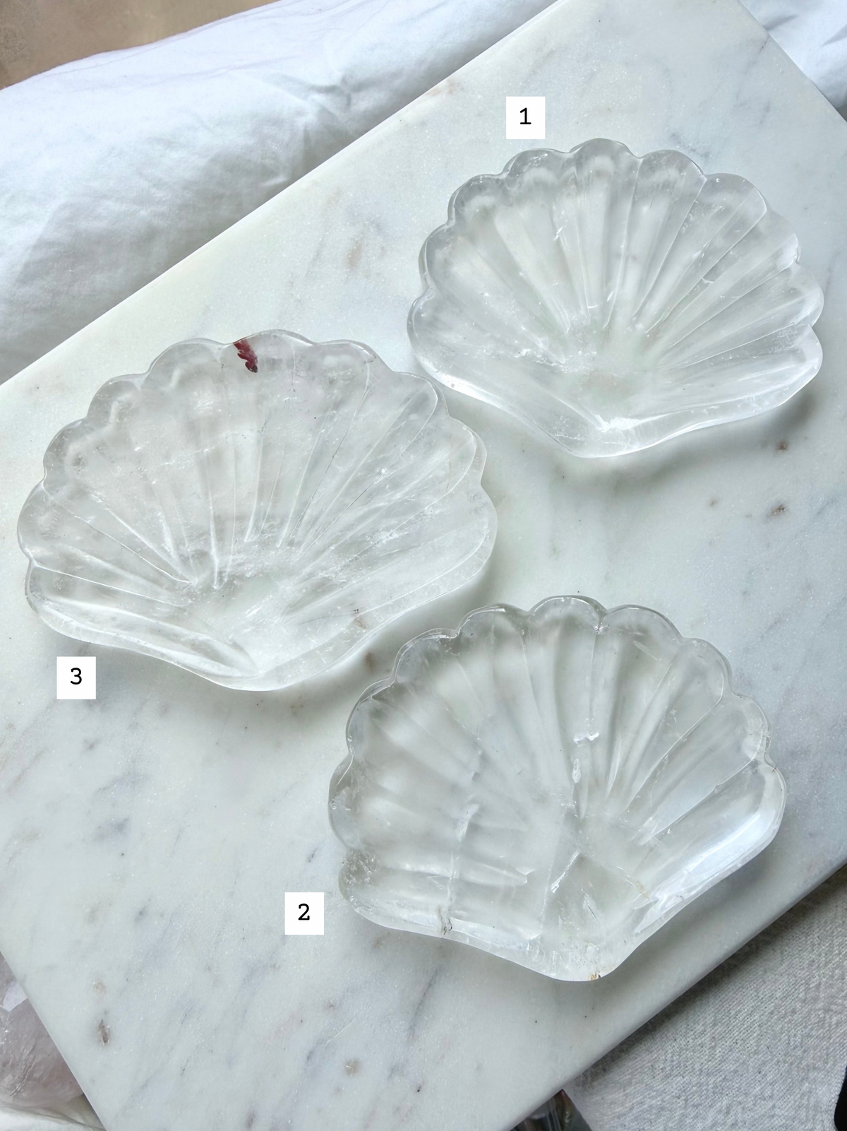 Three Clear Quartz shell bowls with translucent white crystal, scalloped edges, and natural mineral variations, marked for easy selection