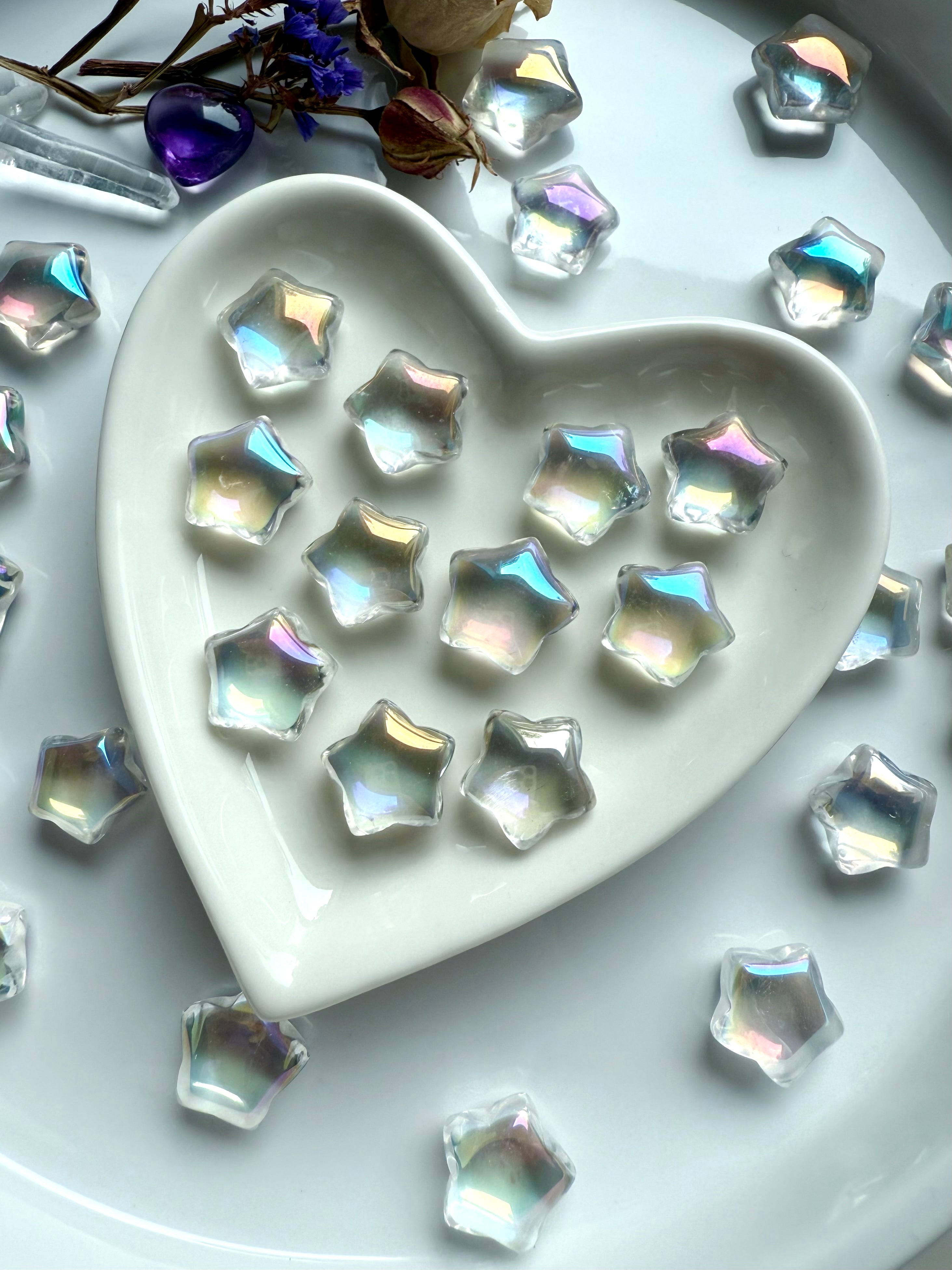 Mini aura quartz stars with rainbow flash displayed in white ceramic heart dish with dried flowers — crystal carvings for chakra healing and décor