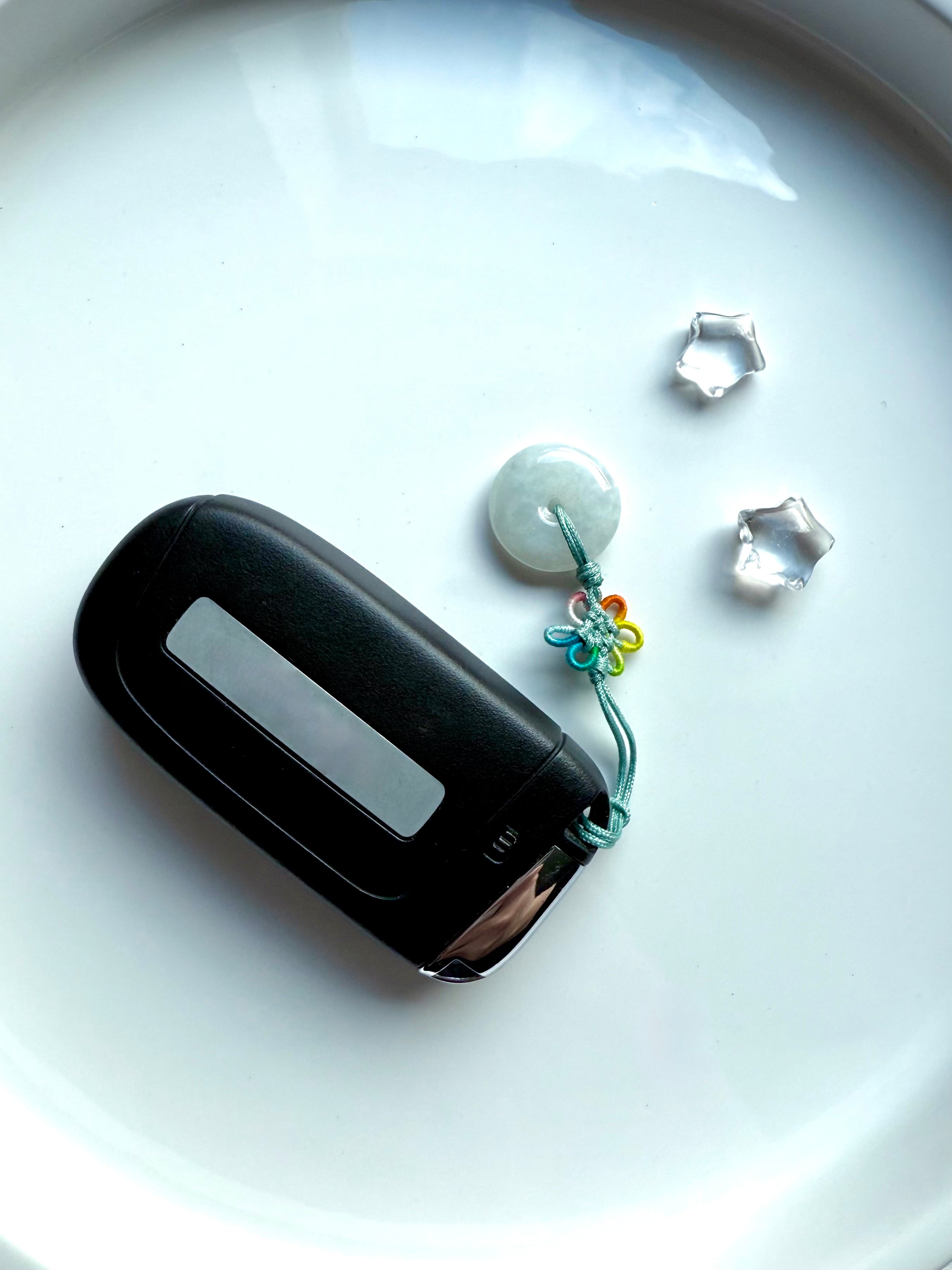 Jade peace buckle charm with rainbow lucky knot used as a car fob keychain, shown on a white ceramic plate