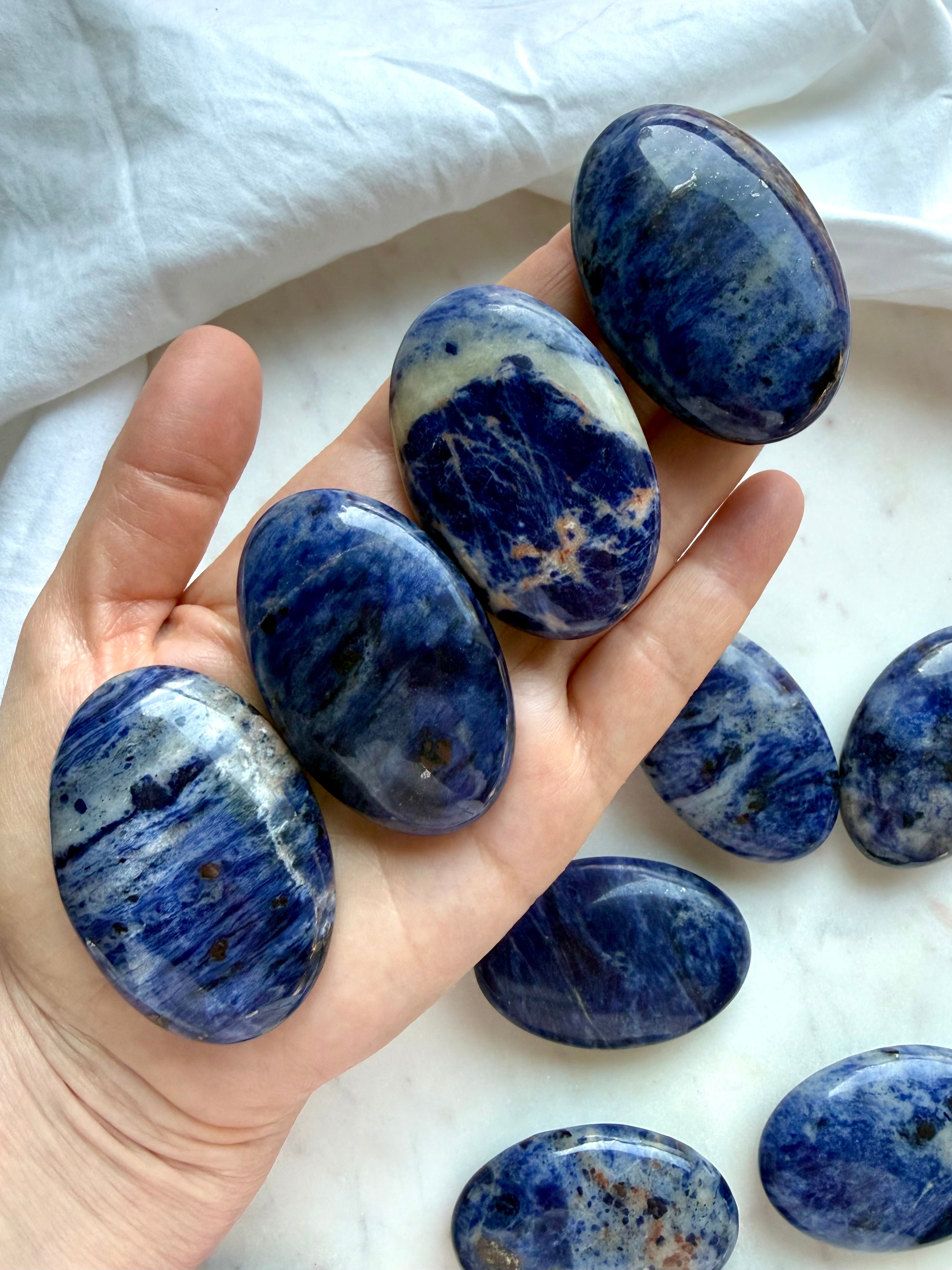 Blue Sodalite palm stones held in hand showing polished oval shape, size, and natural pattern variation