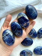 Blue Sodalite palm stones held in hand showing polished oval shape, size, and natural pattern variation