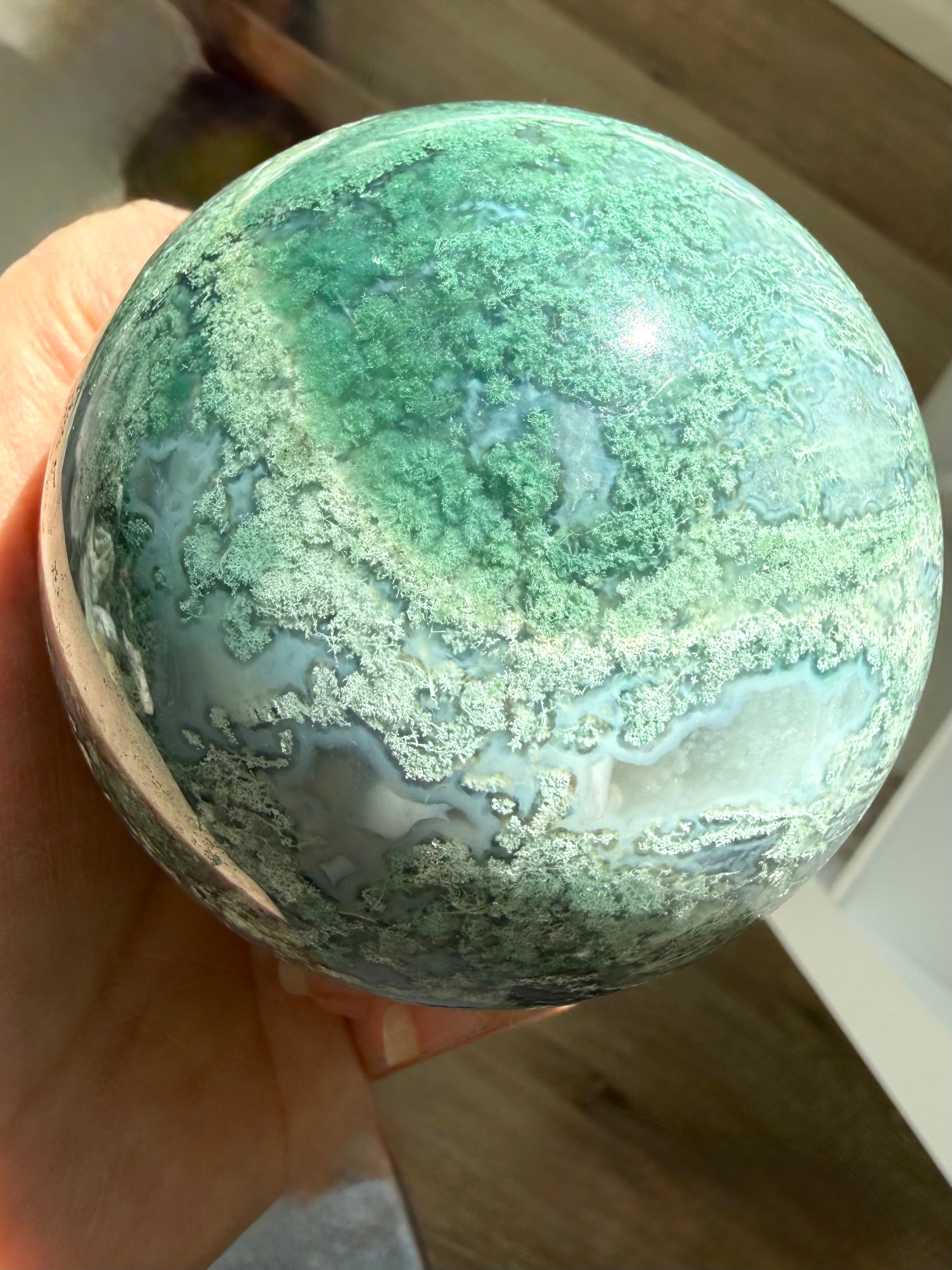 Lacy Moss Agate sphere in bright sunlight showing vivid green patterns, Quartz veins, and natural crystal details