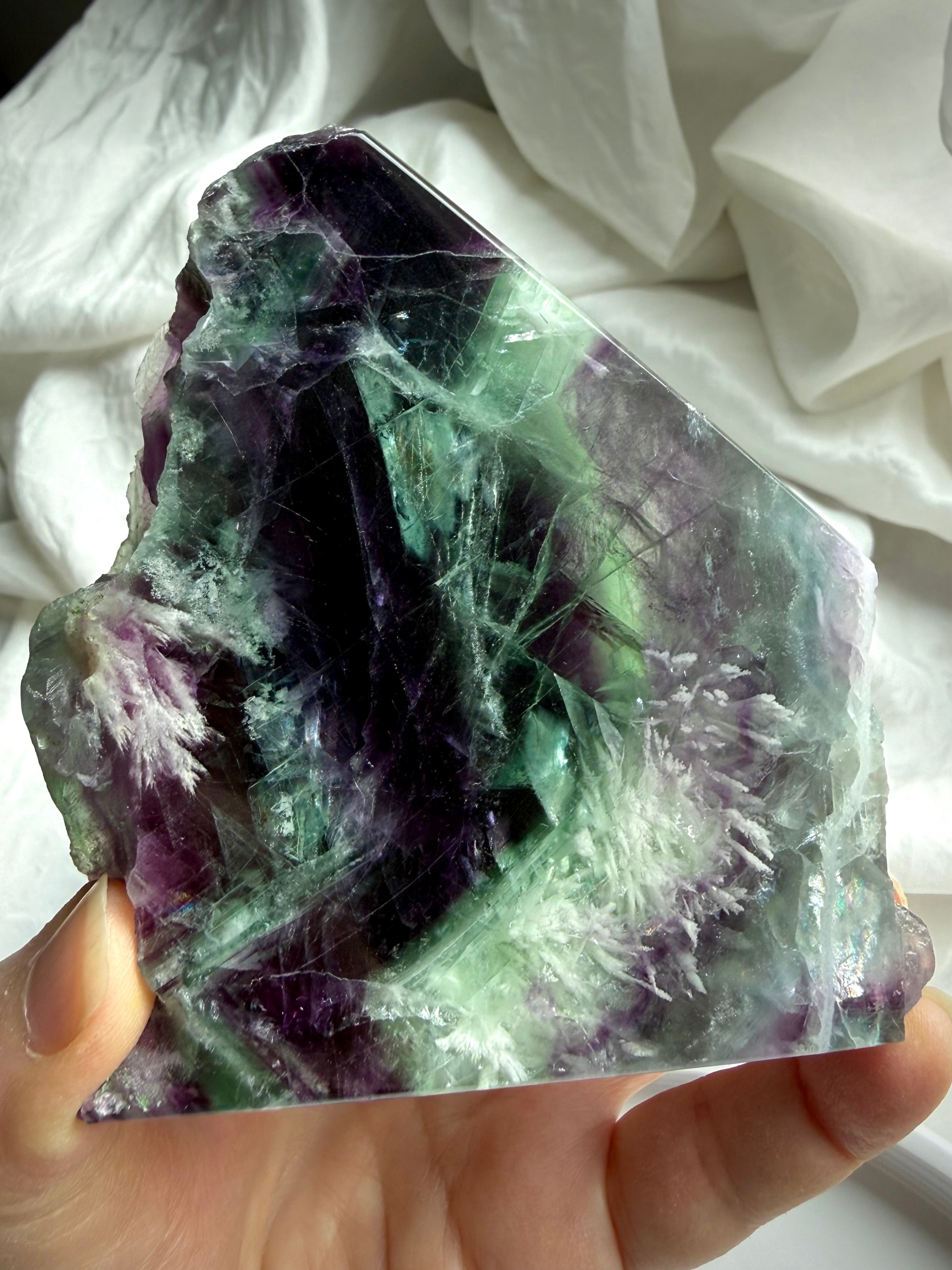 Polished fluorite slab photographed in natural light highlighting layered green and violet color zoning with rainbows