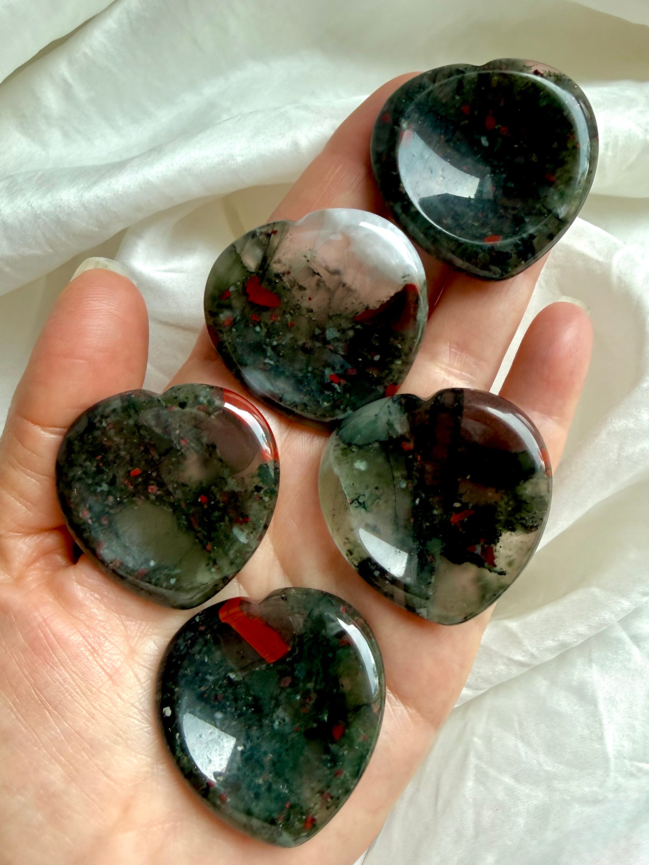 five bloodstone hearts shown on hand with rich green tones and vivid red inclusions, grounding crystal for strength focus and vitality 