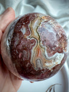 Textured agate sphere showing layered natural banding, soft mauve tones, and druzy cave formation