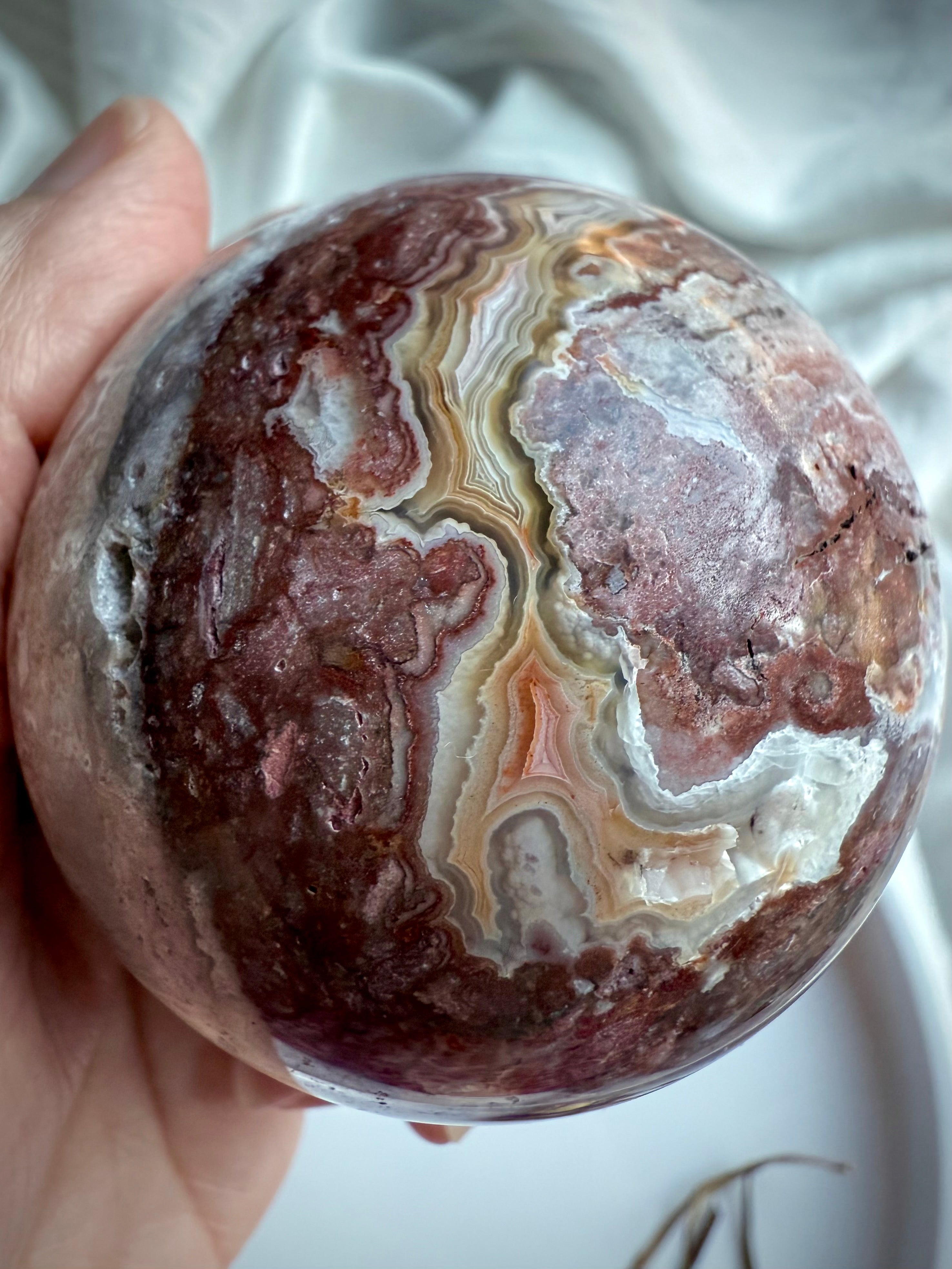 Textured agate sphere showing layered natural banding, soft mauve tones, and druzy cave formation
