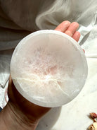 top view of selenite charging bowl on hand showing natural crack and internal mineral patterns, white crystal cleansing bowl