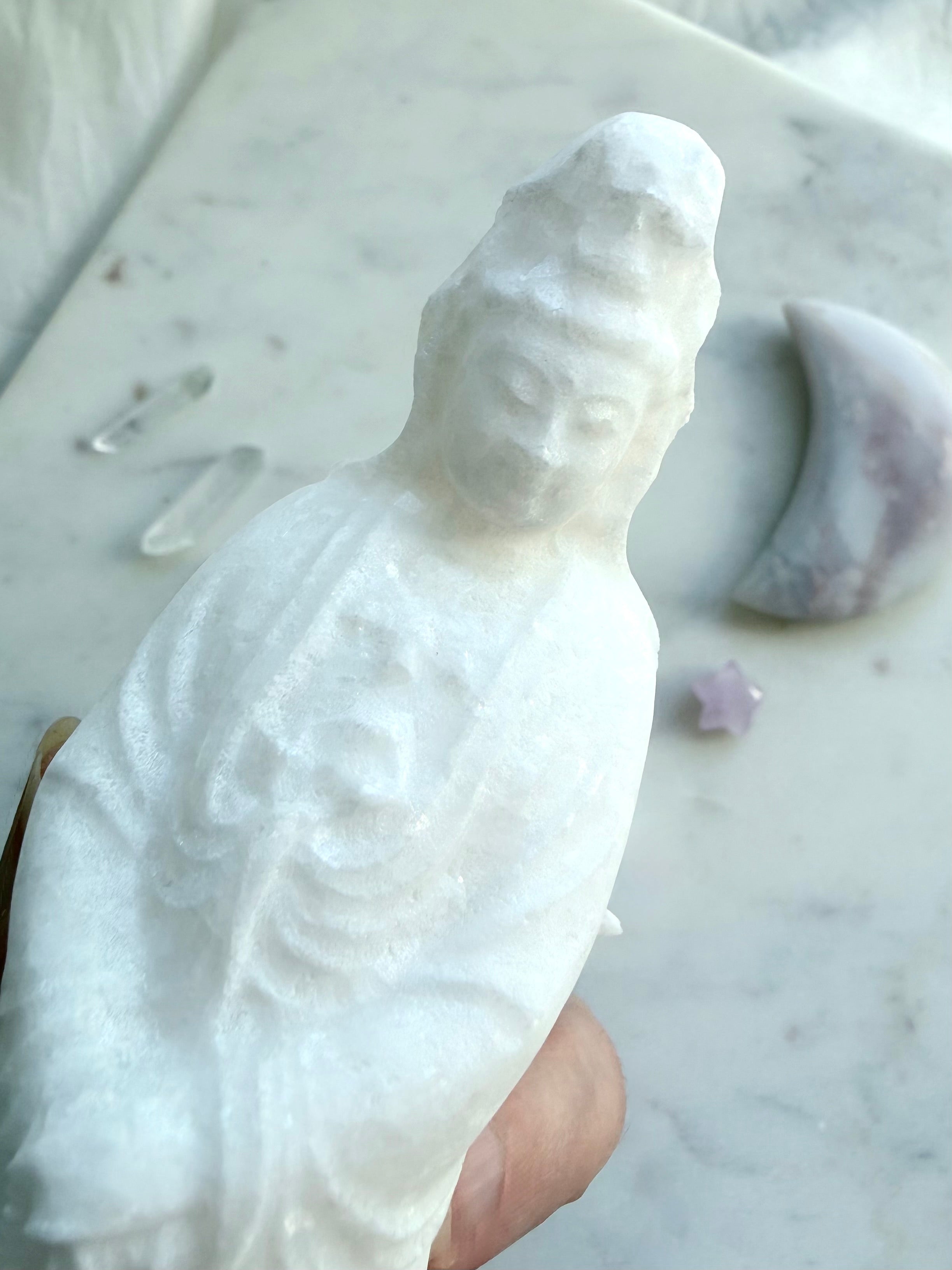 Close up White Jade Quan Yin carving held in hand beside crystal decor for scale and detail