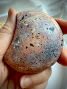 Polished Ocean Jasper moon in warm pink and tan tones with starburst orbicular markings held in hand