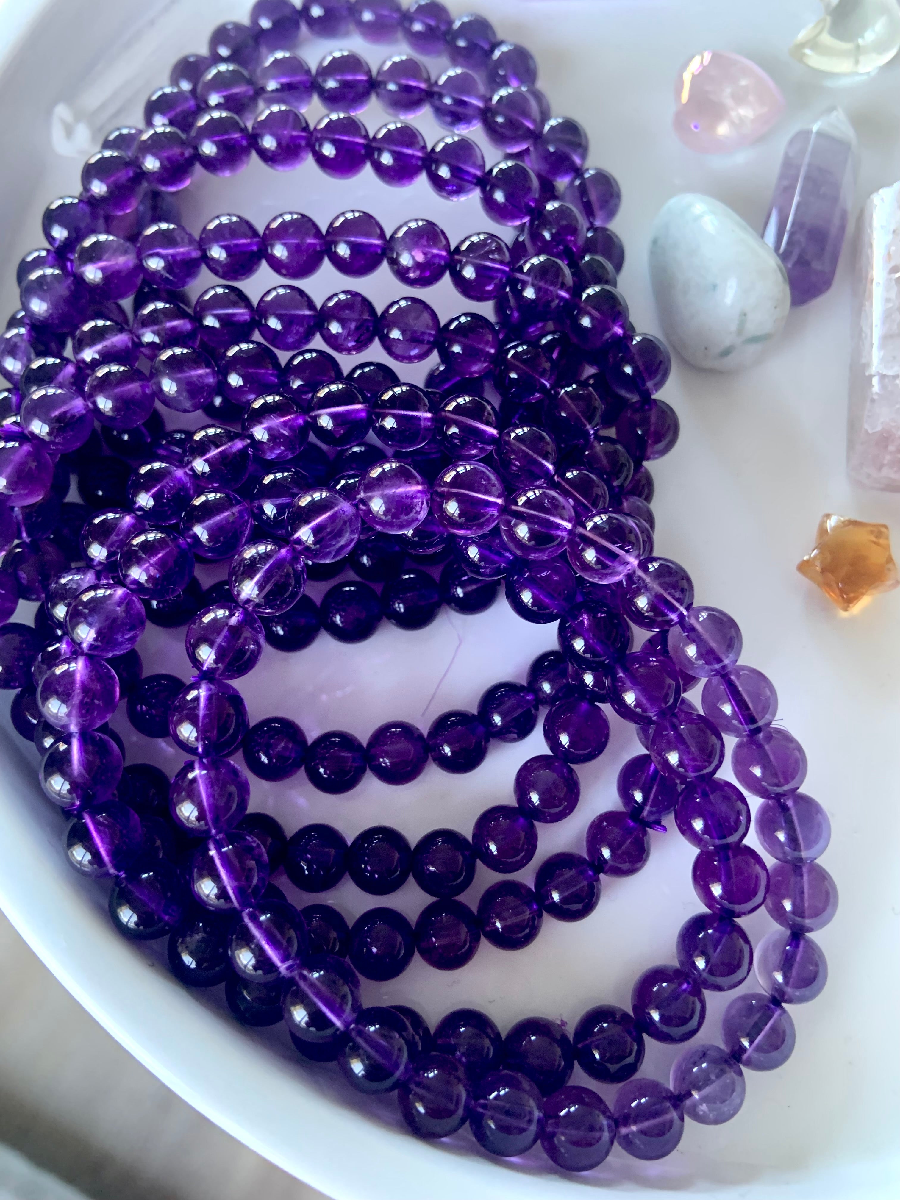 An array of high quality deep purple amethyst beaded bracelets on a white plate with other mini crystals in the background