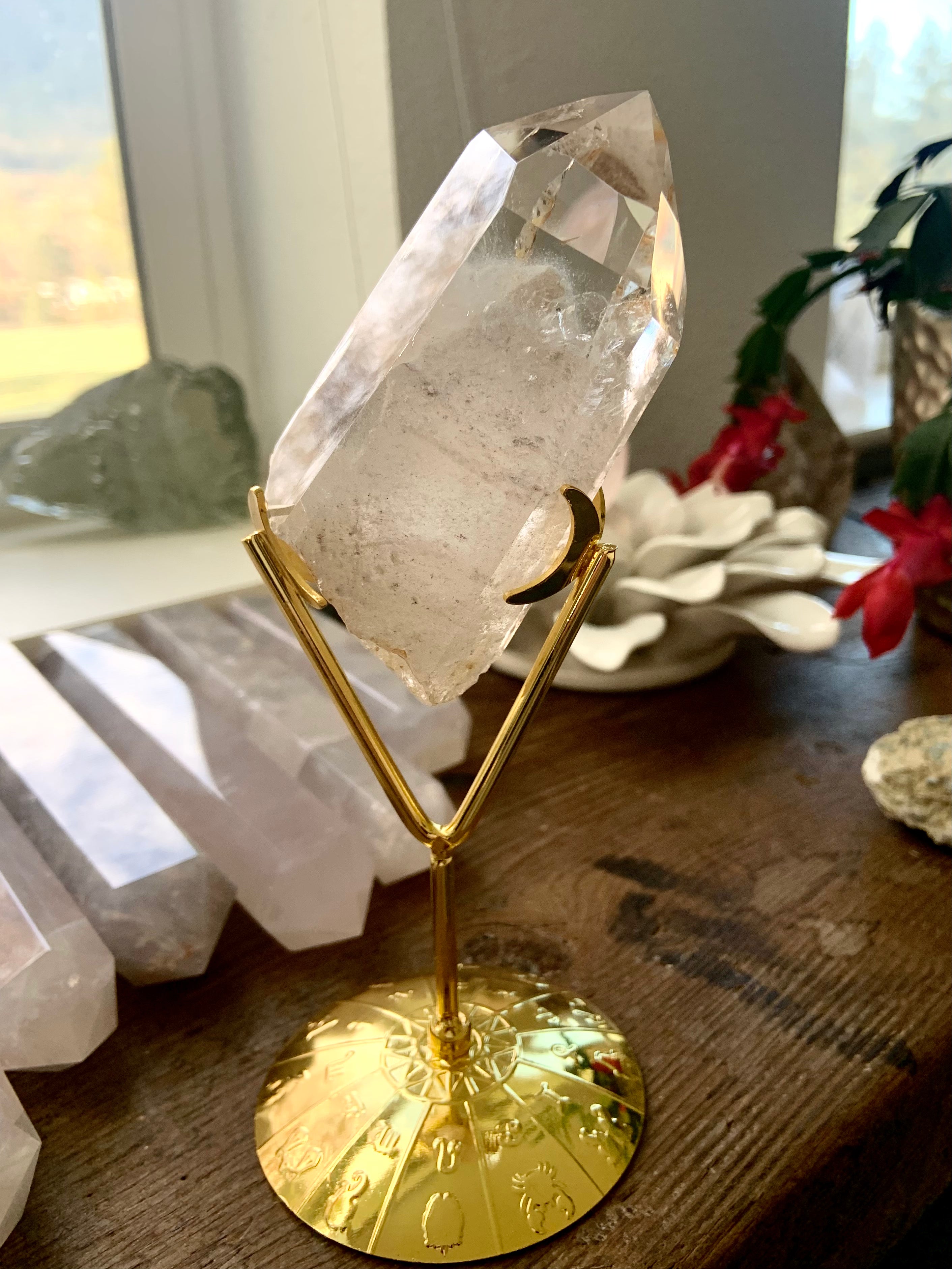 Crystal display stand with zodiac wheel design holding a raw phantom quartz point — elegant gold crystal holder for decor or altar display