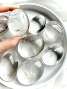 clear quartz palm stones on white tray with one held to the light showing high clarity and natural inclusions