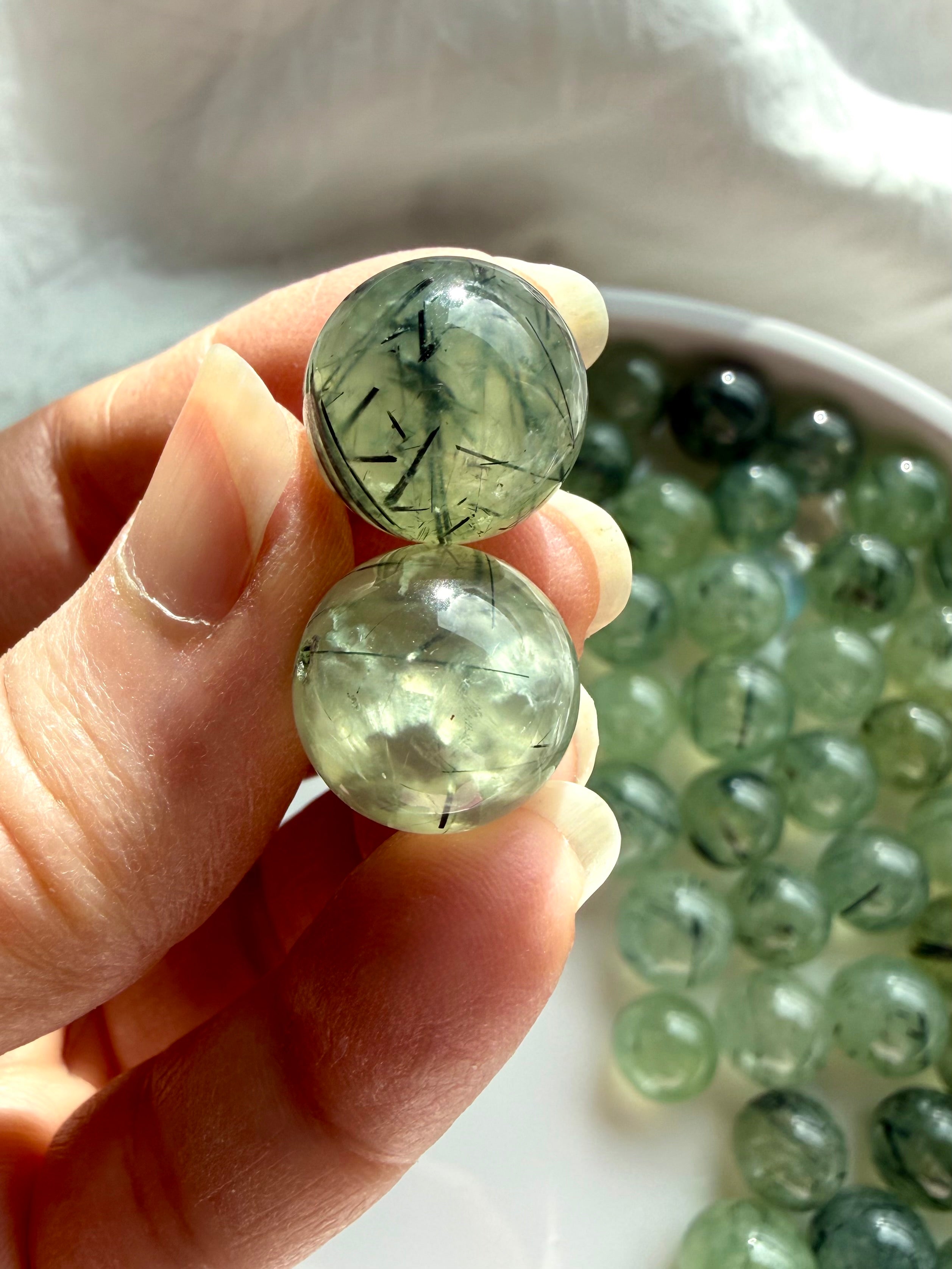 two prehnite mini spheres held between fingers showing clarity and internal inclusions