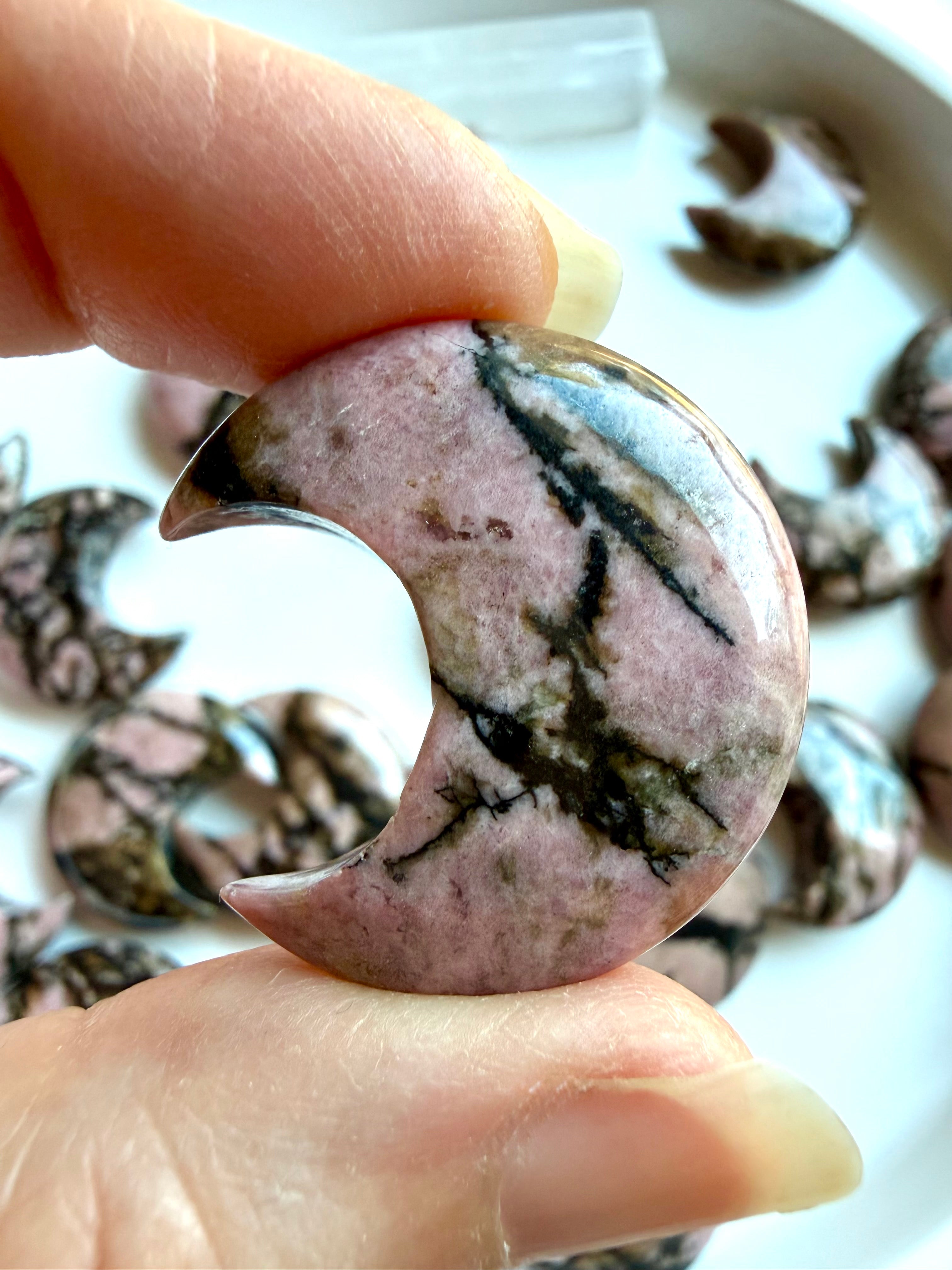 Rhodonite crescent moon crystal held between fingers showing glossy polish and natural pink and black patterns