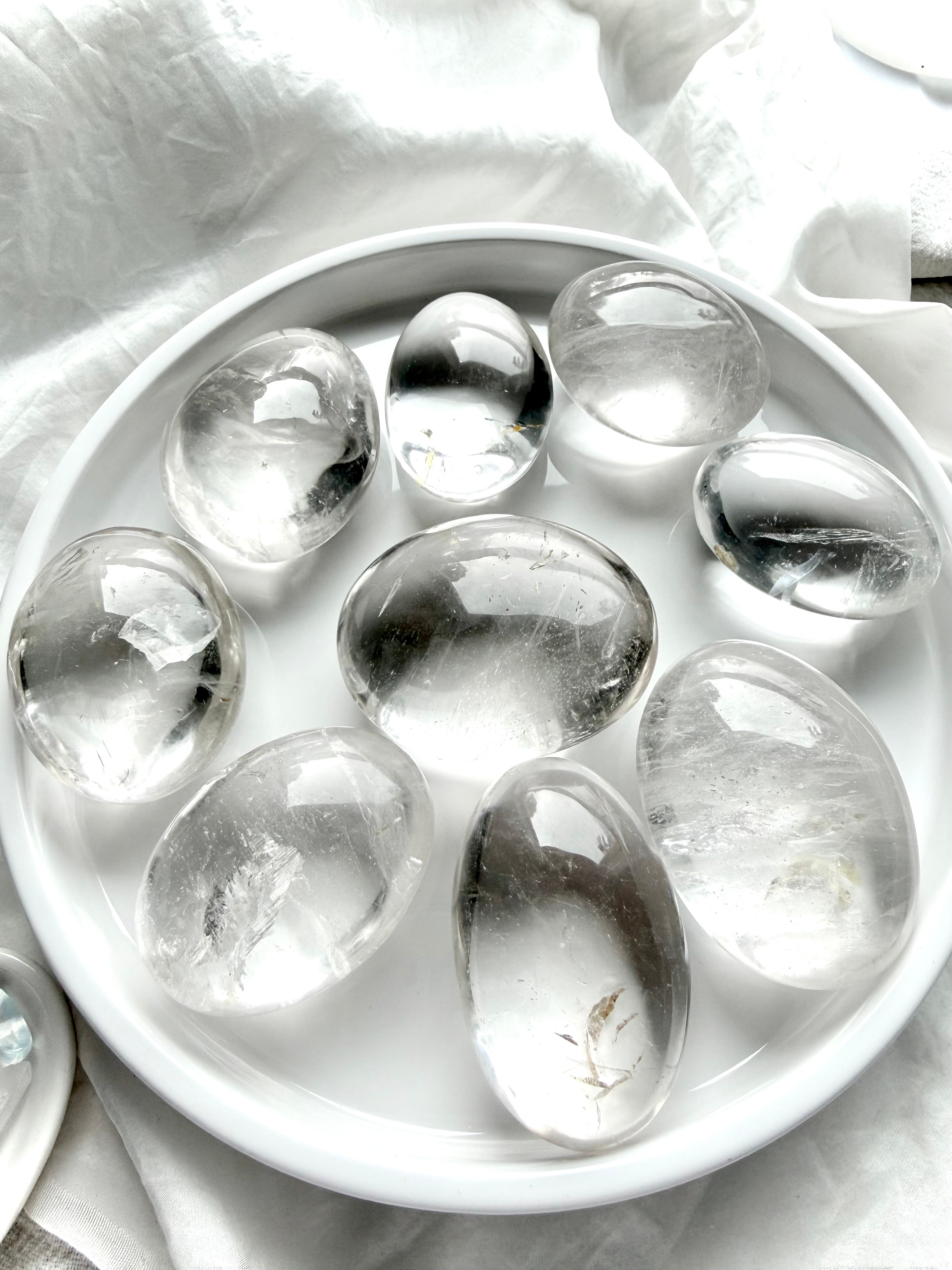 clear quartz palm stones arranged on white tray showing high clarity, natural inclusions, and polished finish