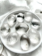 clear quartz palm stones arranged on white tray showing high clarity, natural inclusions, and polished finish