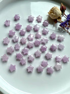 Flat lay of glossy pink Kunzite mini stars with dried rose and purple statice flowers — high-vibe heart chakra altar decor.
