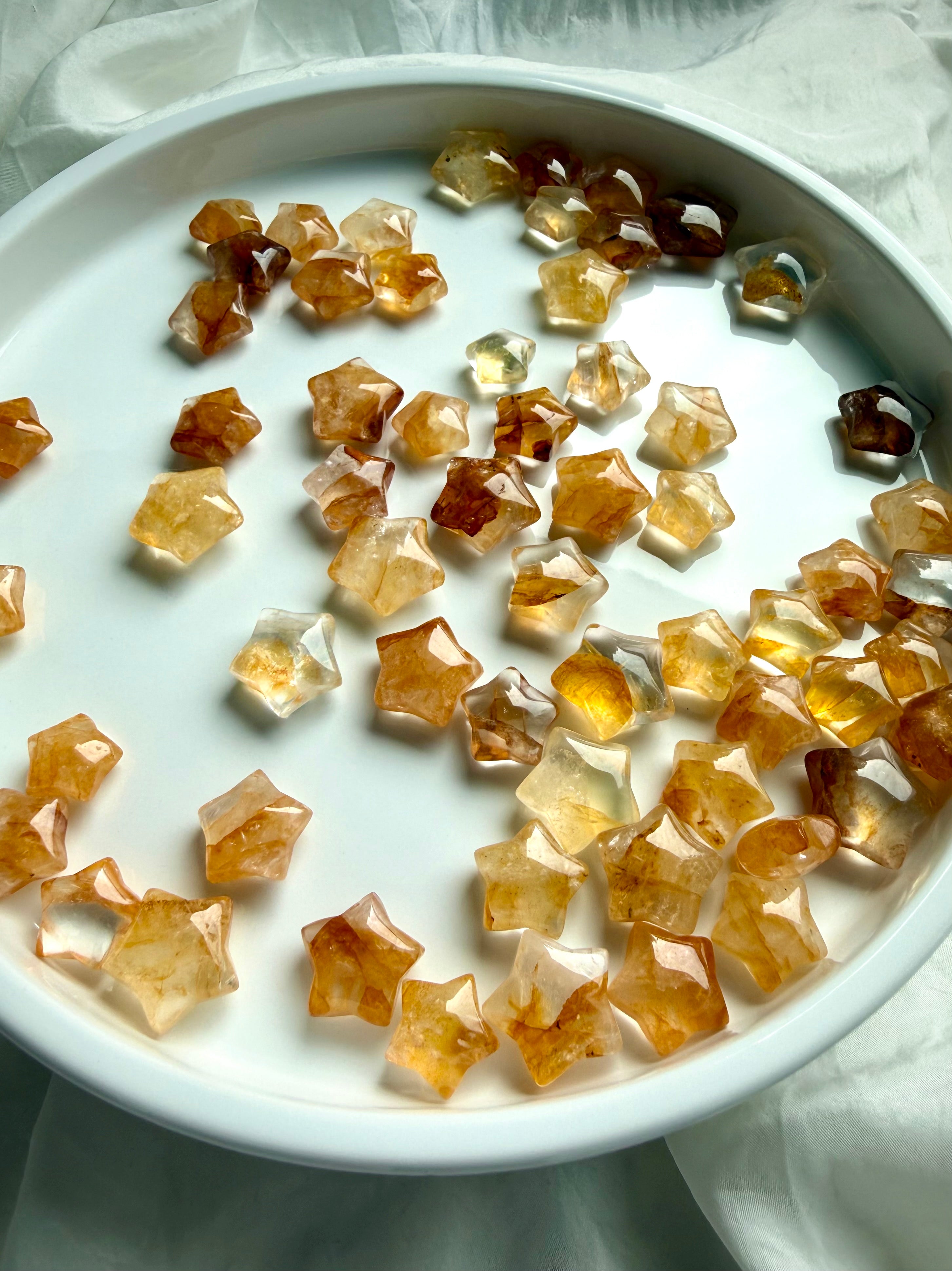 Golden Healer Quartz stars on white crystal plate showing natural color variation and polished star shapes